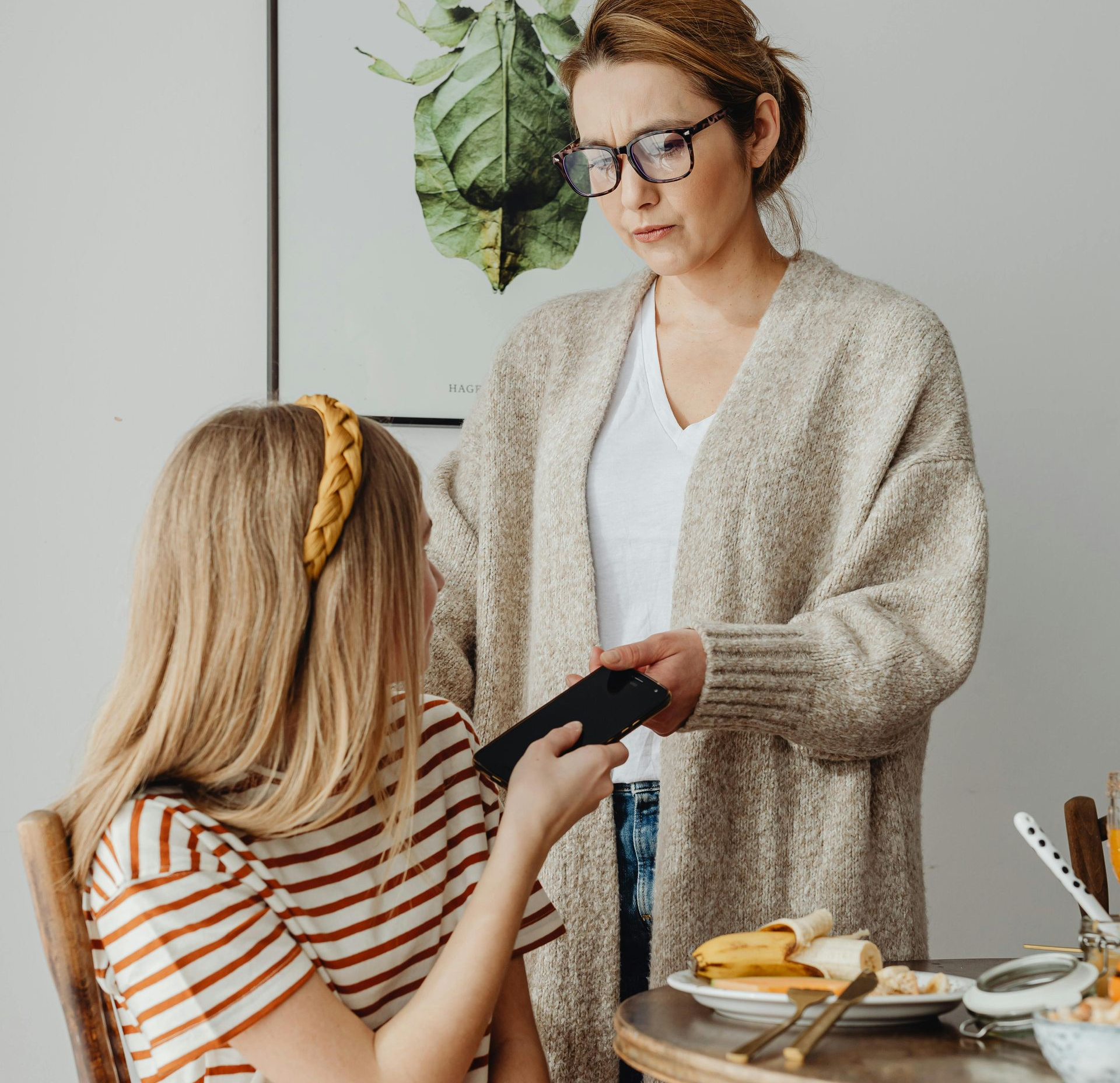 Mother handing a phone to girl at the breakfast table.