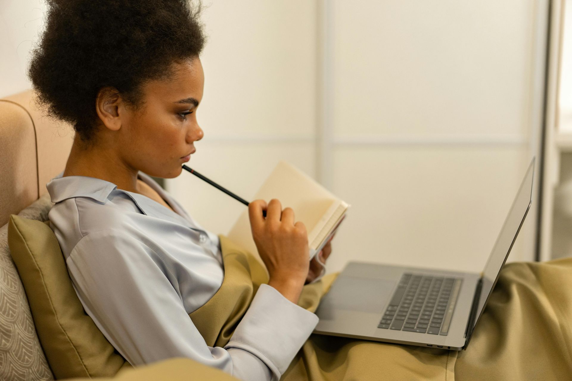 Person holding a notebook on a couch beside an open laptop