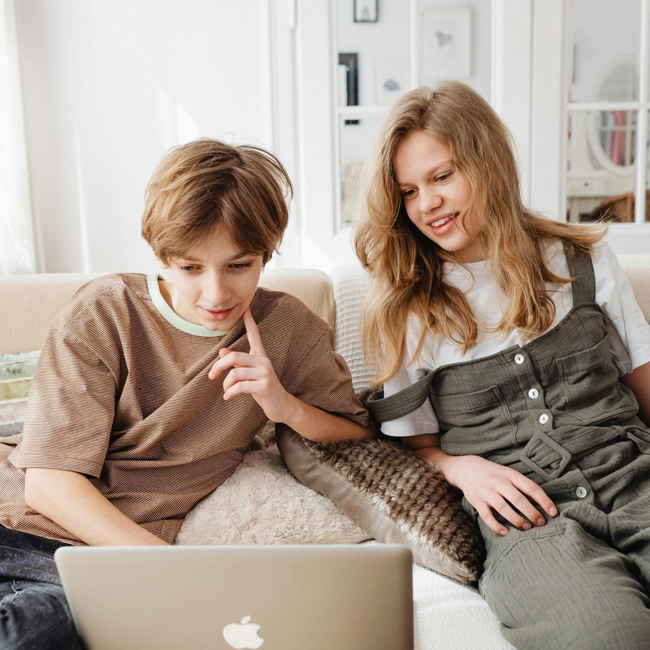 A boy and a girl are sitting on a couch looking at a laptop.