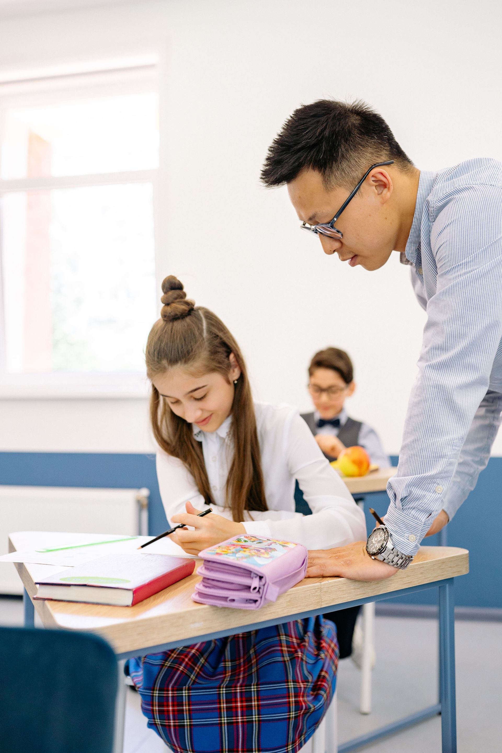 Teacher helping a student write at a desk in a classroom