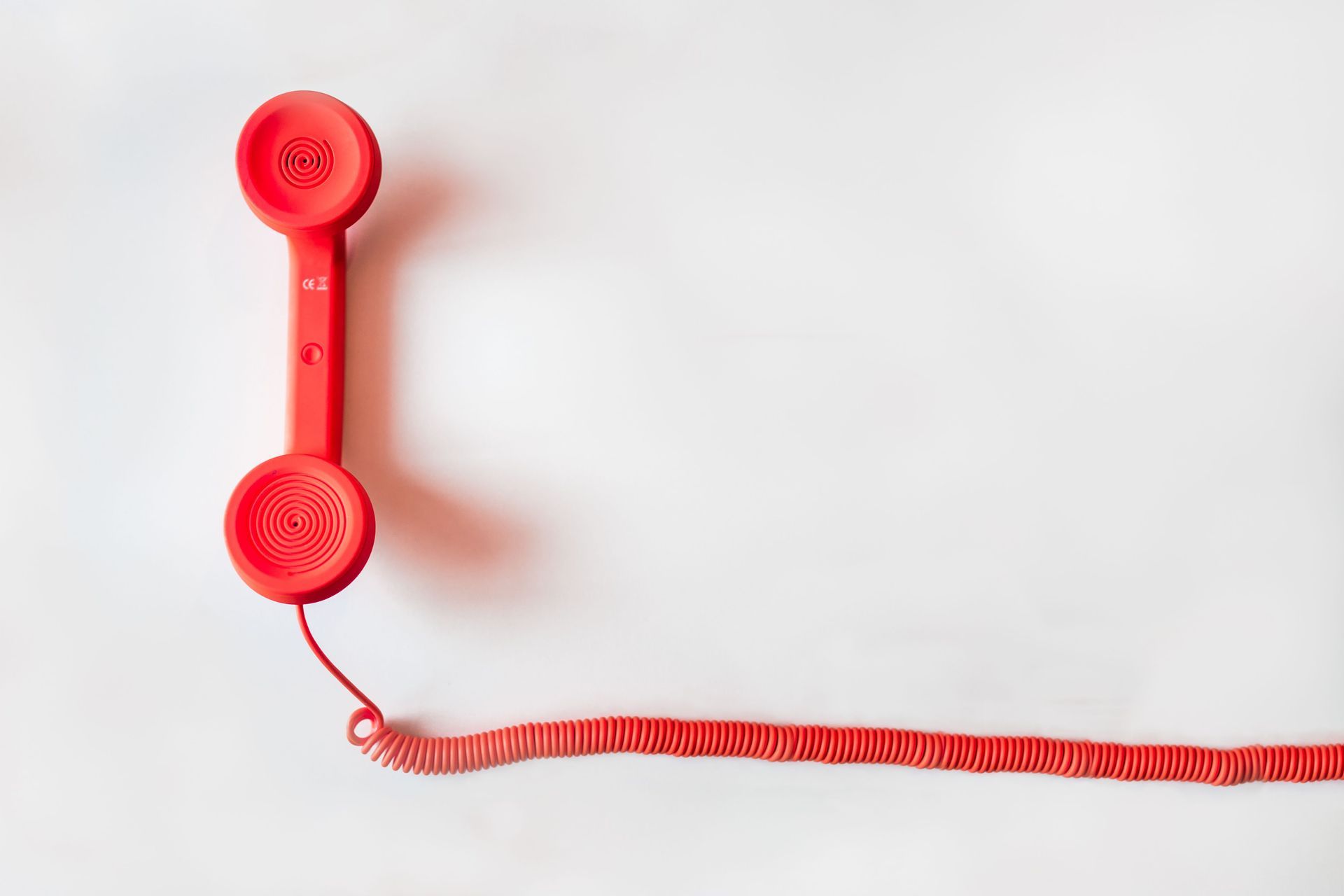 Red telephone handset on a white background with a coiled cord extending to the right
