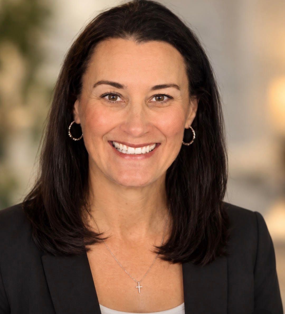 Smiling woman with dark hair in a black blazer against a softly blurred background