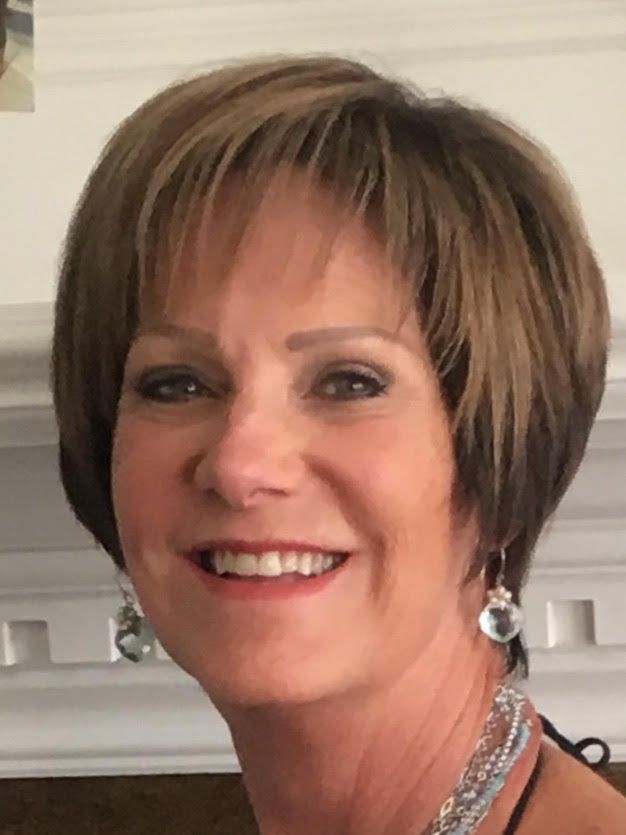 Smiling woman with short brown hair and earrings, standing indoors near a white fireplace mantel