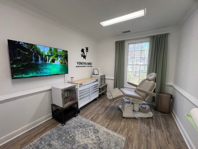 Bright therapy room with wall-mounted TV, recliner, cabinet, and window with sheer curtains