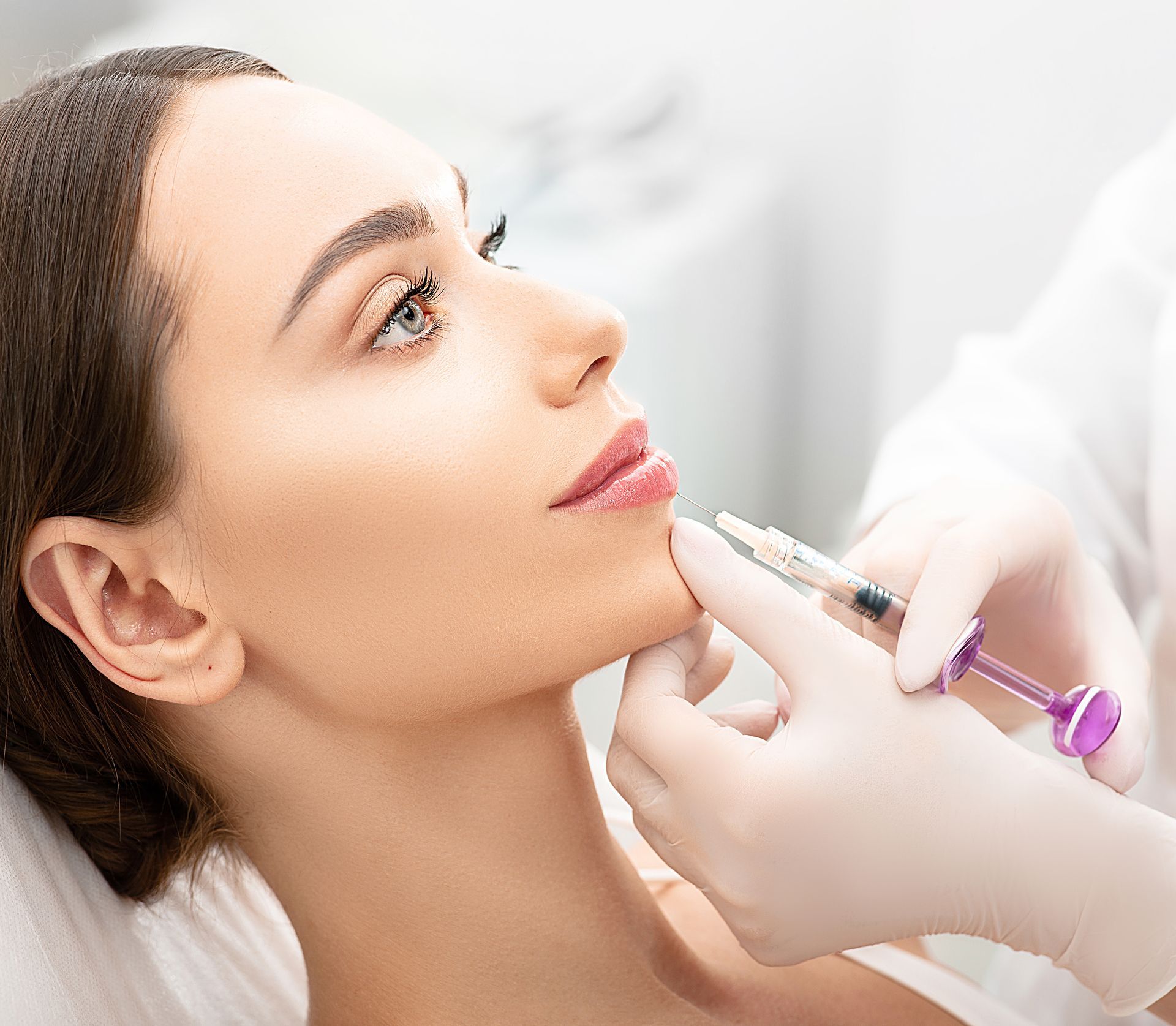 Cosmetologist injects facial filler into a woman’s chin in a bright clinic