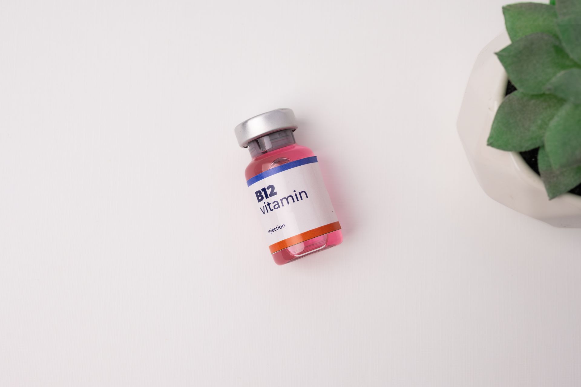 Small pink medicine vial with silver cap on a white surface beside a green plant.