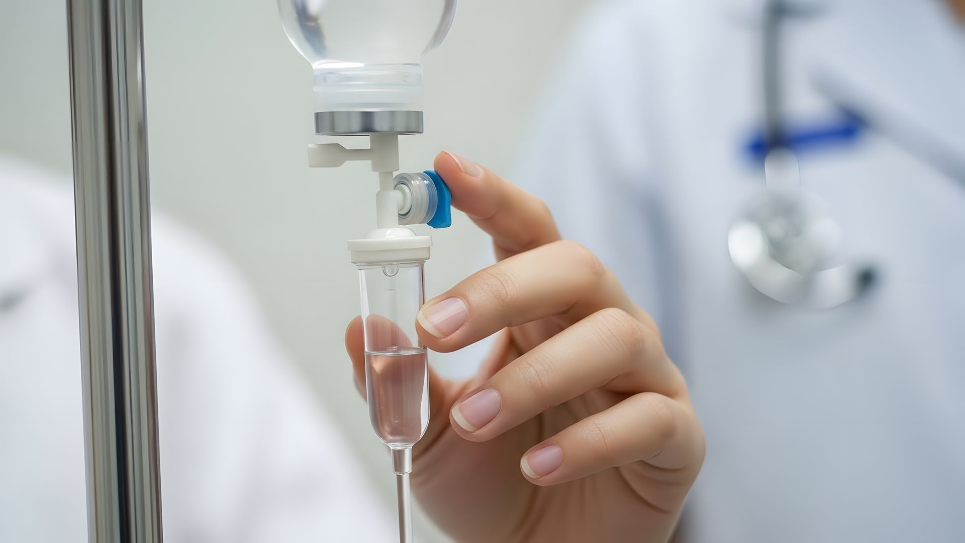 Nurse adjusting an IV drip beside a patient’s hand in a hospital setting