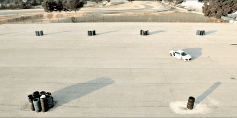 A white car driving on a concrete course with obstacles. Daytime, aerial view.