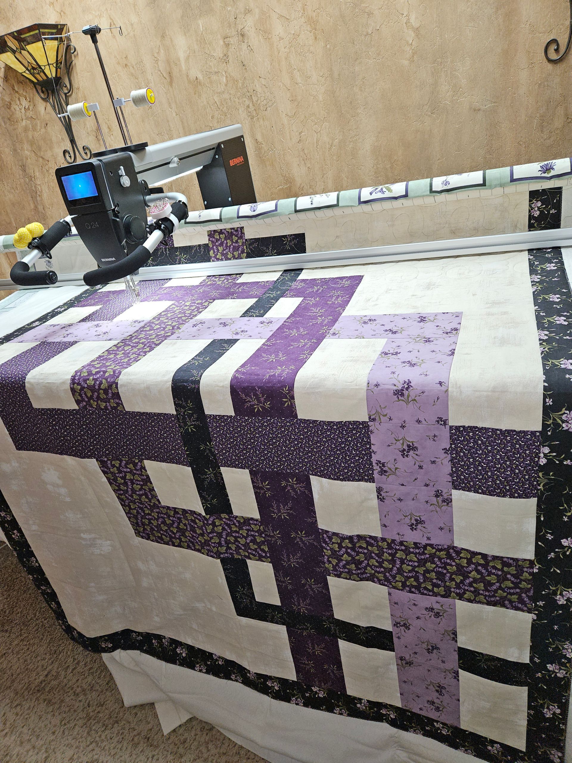 A purple and white quilt is being made on a machine.