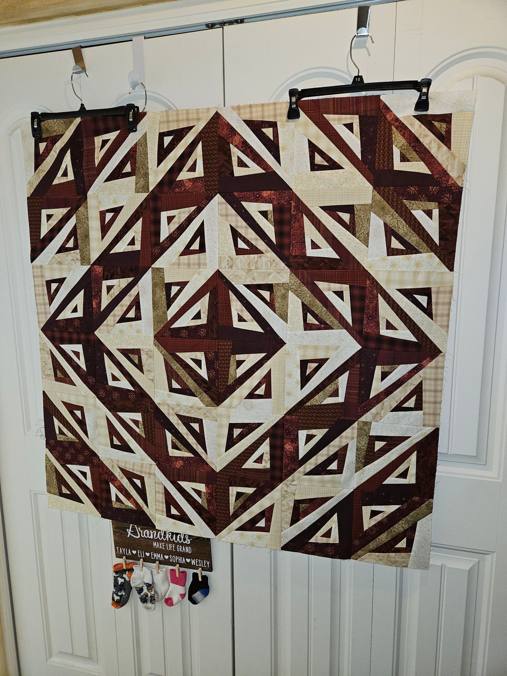 A brown and white quilt is hanging on a white door.