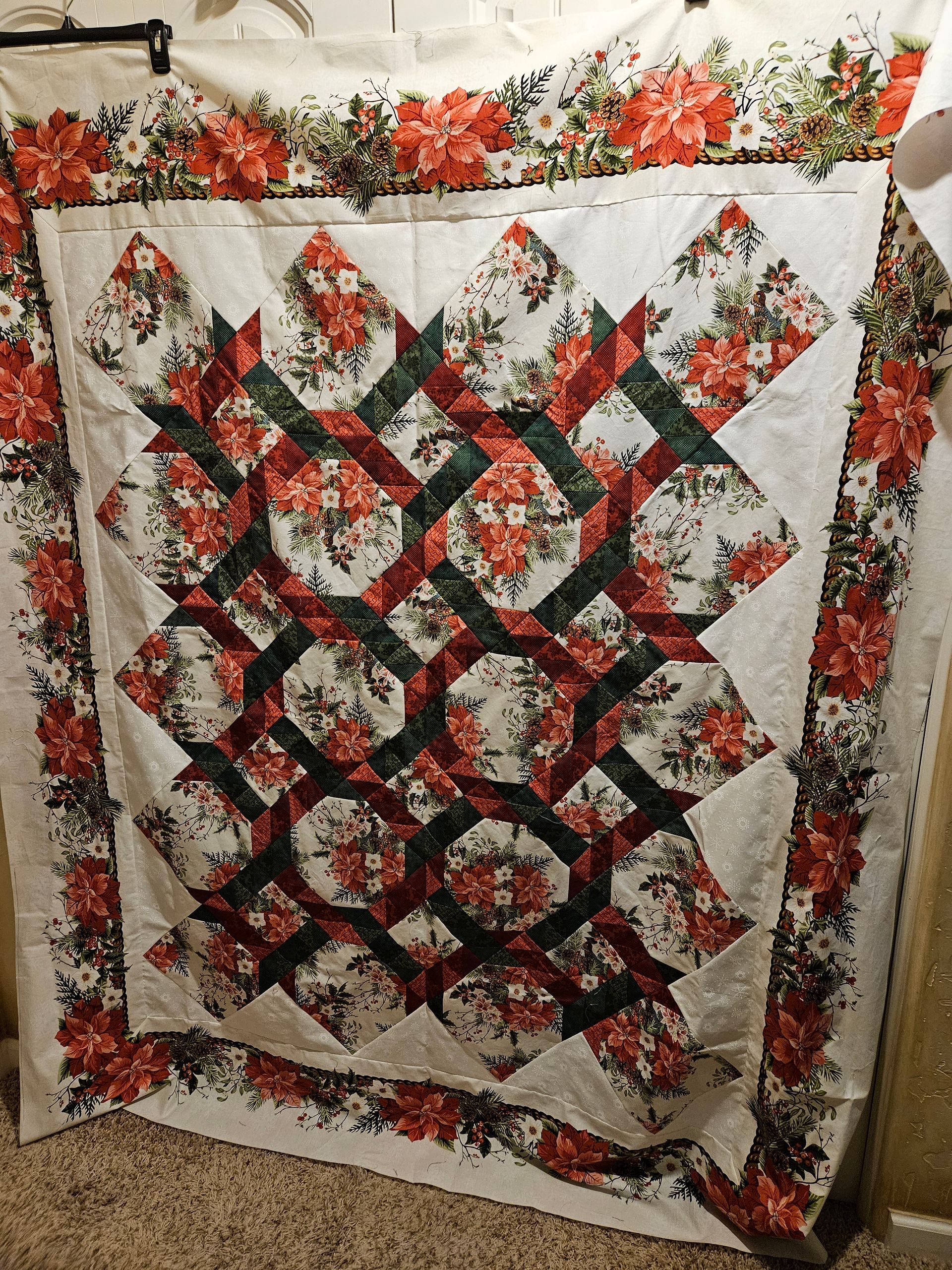 A quilt with red and green flowers on it is hanging on a wall.