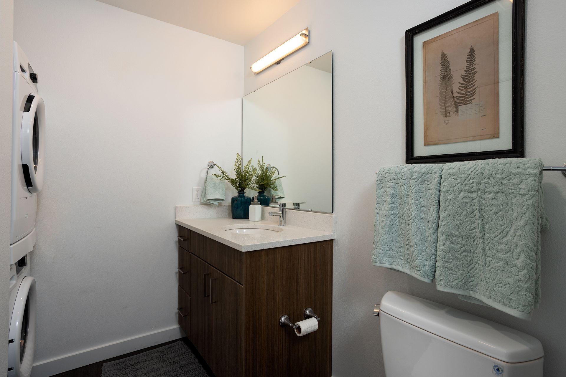 A bathroom with a sink , toilet , mirror and washer and dryer.