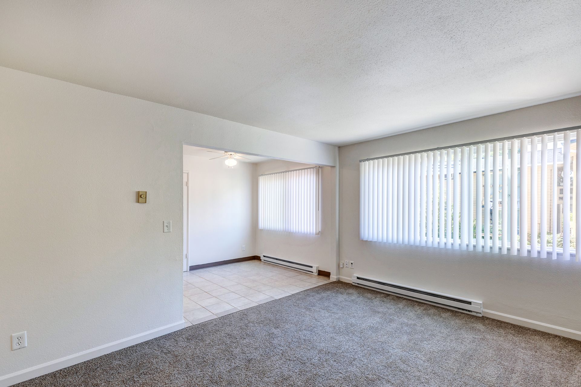 An empty living room with a large window and blinds.