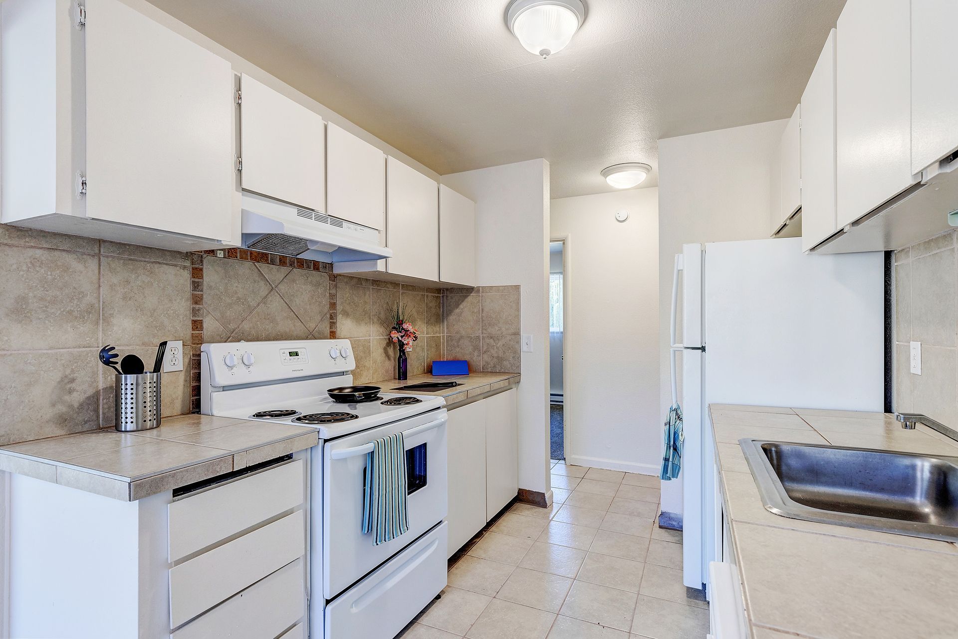 A kitchen with white cabinets , a stove , a refrigerator , and a sink.