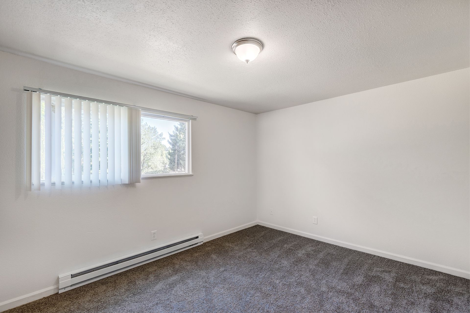 An empty bedroom with a window and blinds.