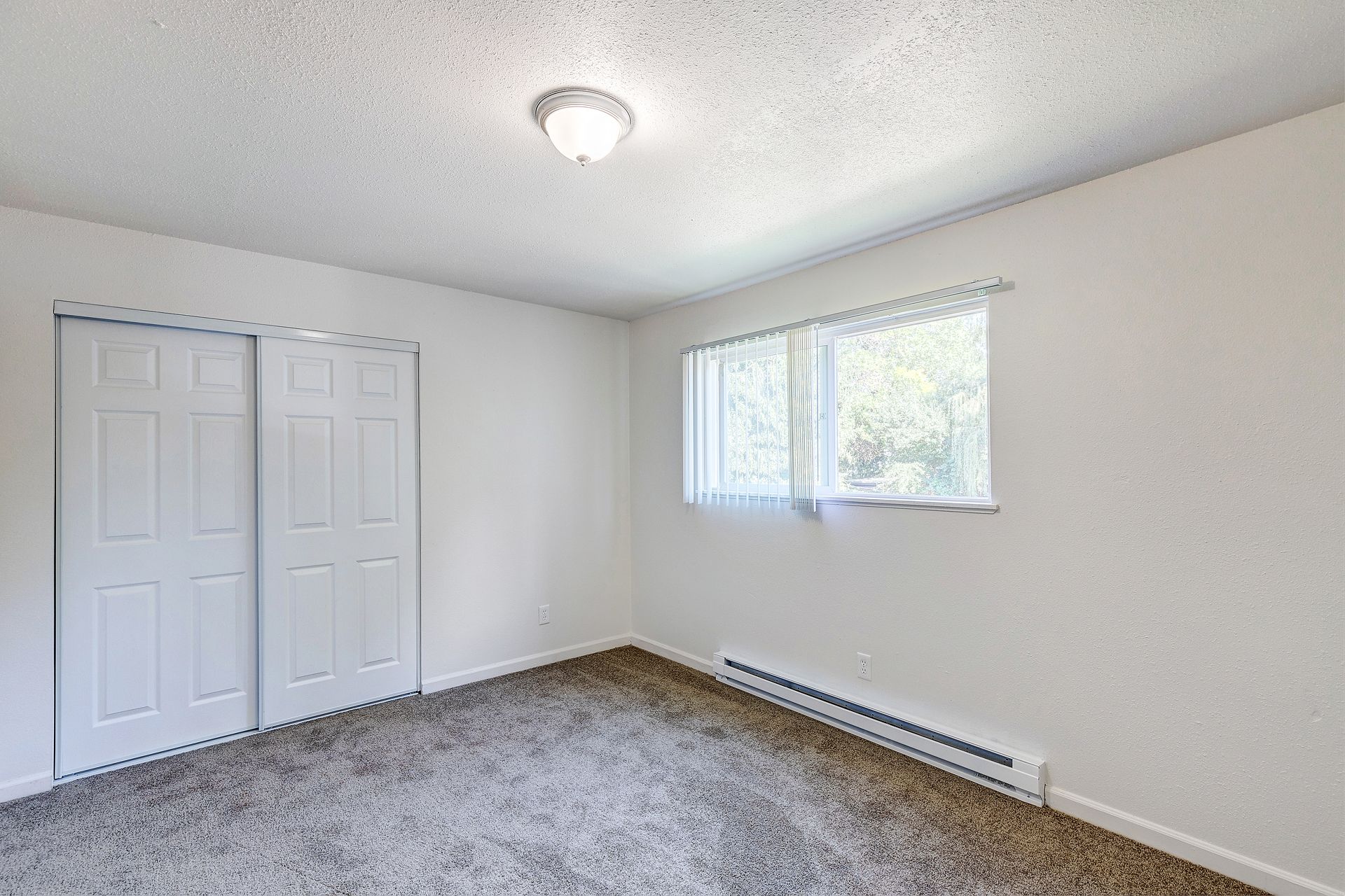 An empty bedroom with a carpeted floor and a window.