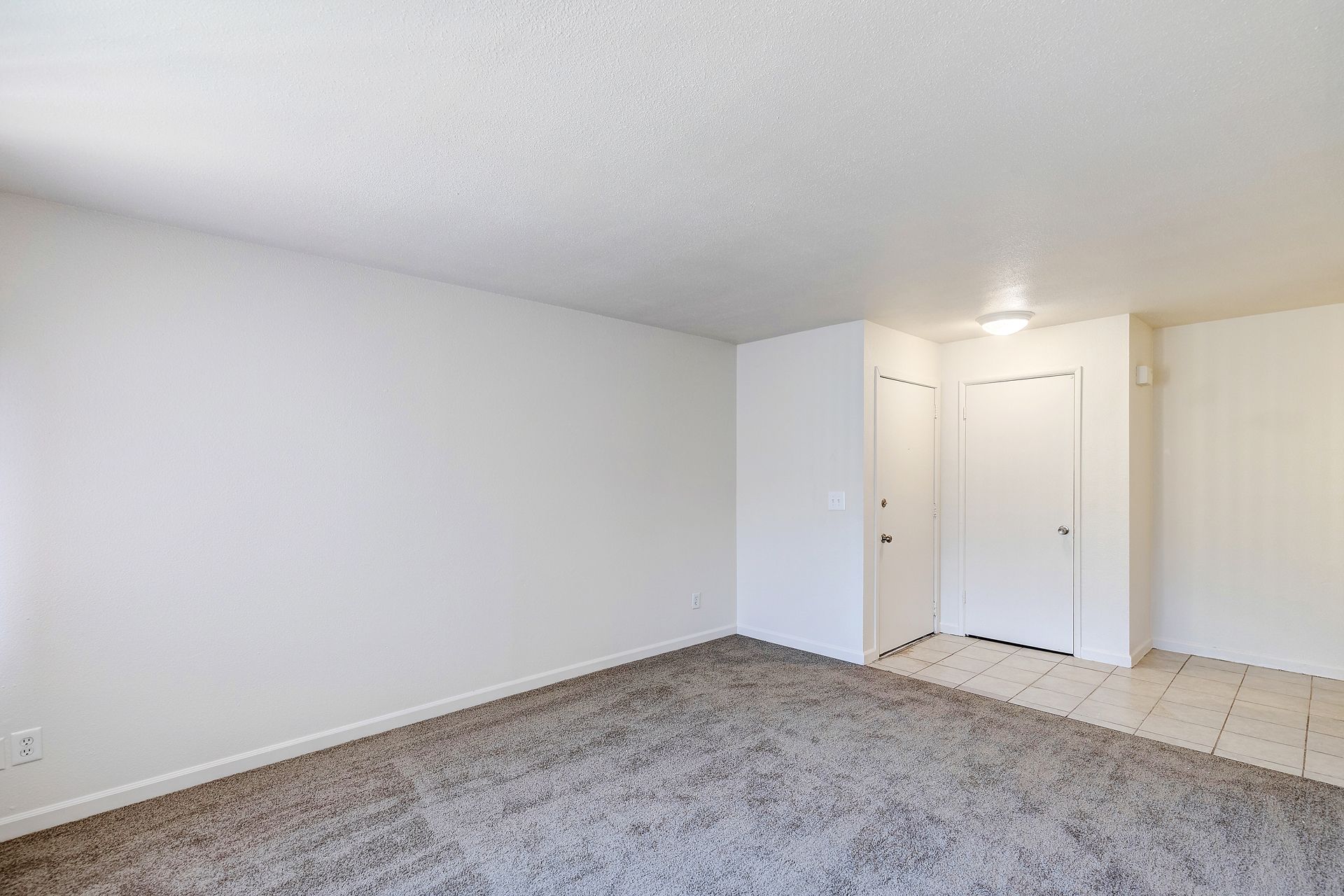 An empty living room with a carpeted floor and white walls.