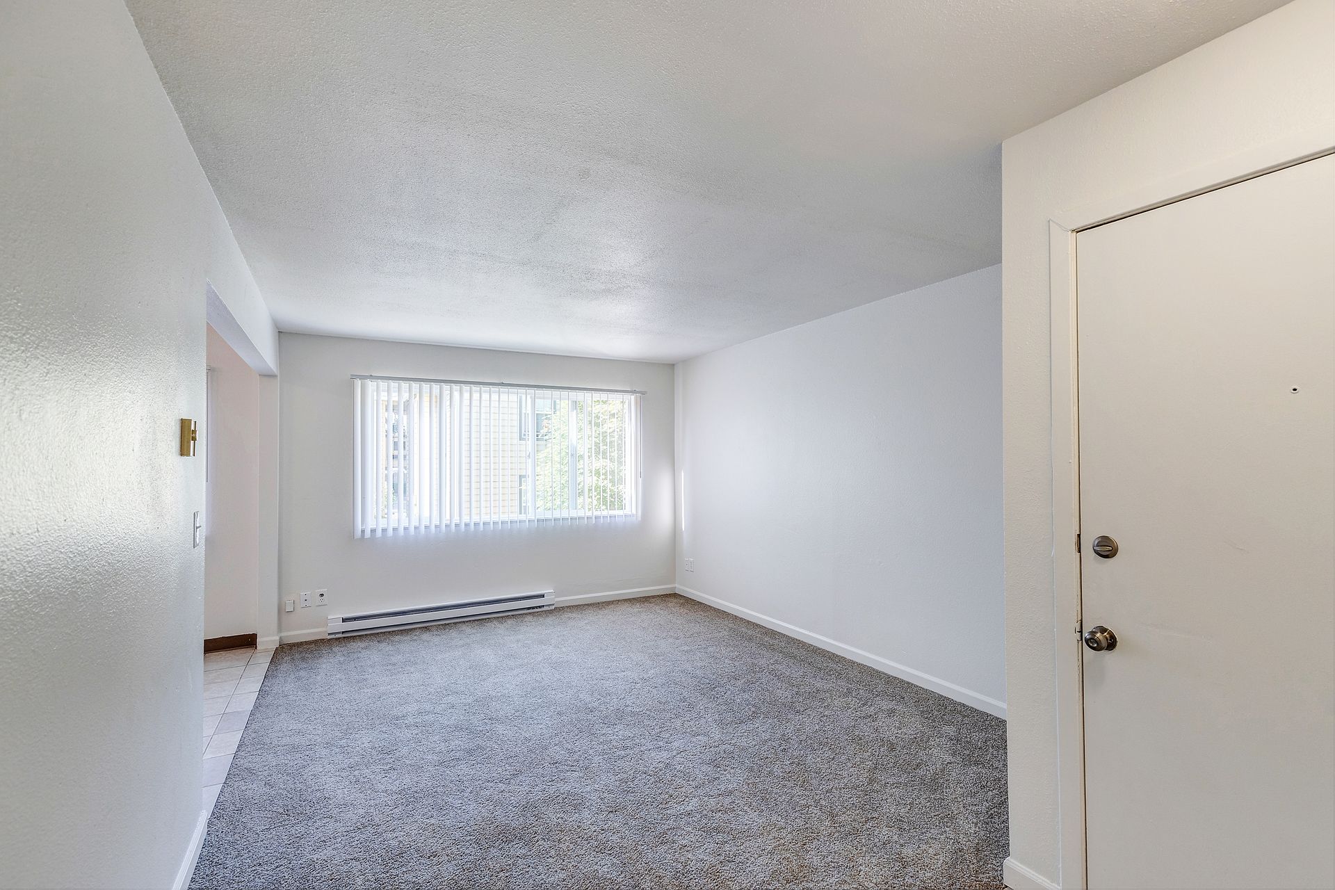 An empty living room with a carpeted floor and white walls.