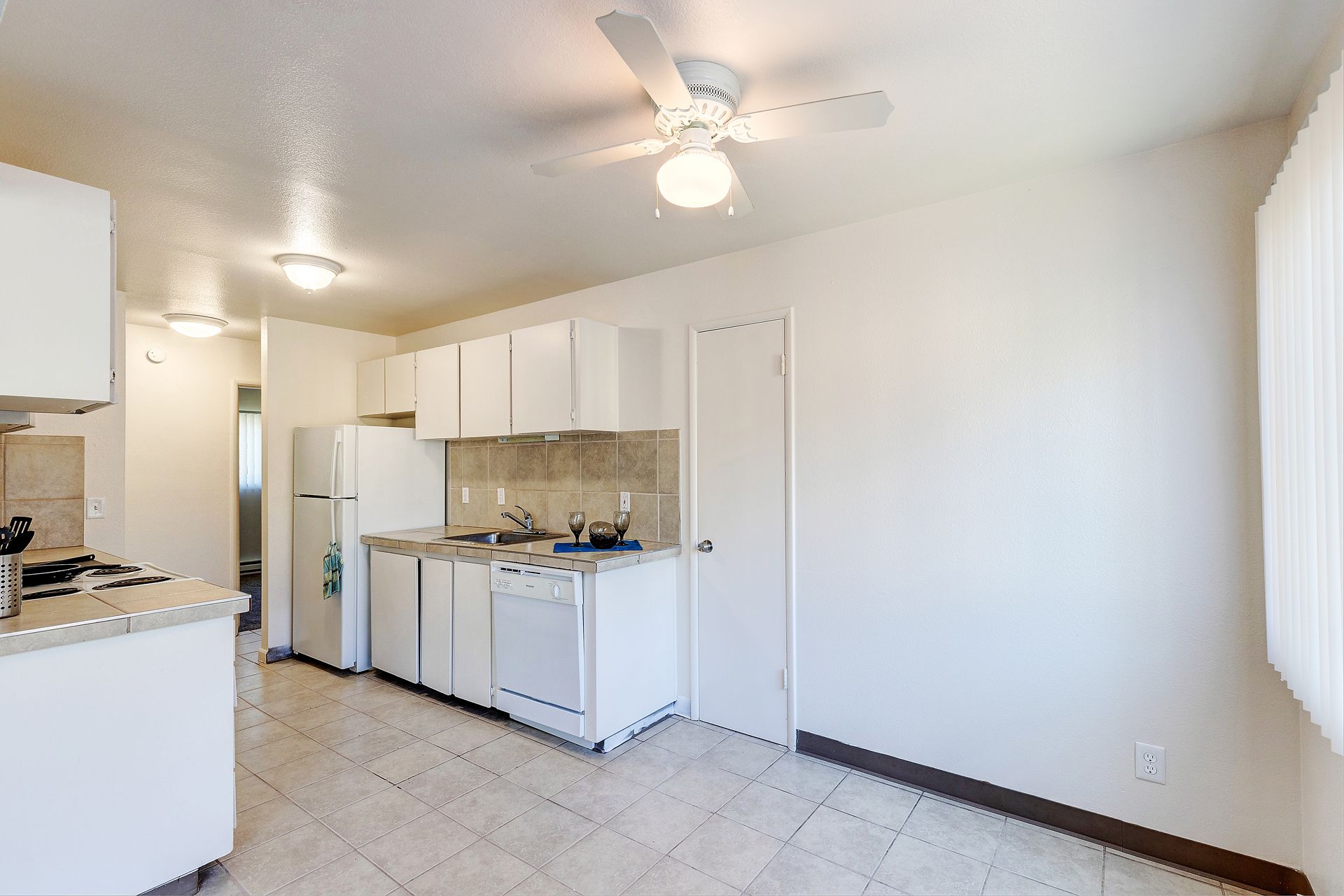 An empty kitchen with white cabinets and a ceiling fan