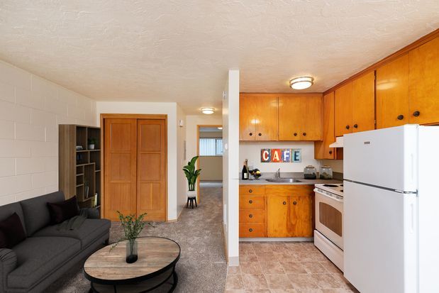 A living room with a table and chairs and a kitchen with a refrigerator and stove
