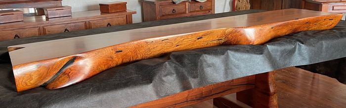 Wooden mallet with orange patterned handle resting on a gray padded surface in a workshop