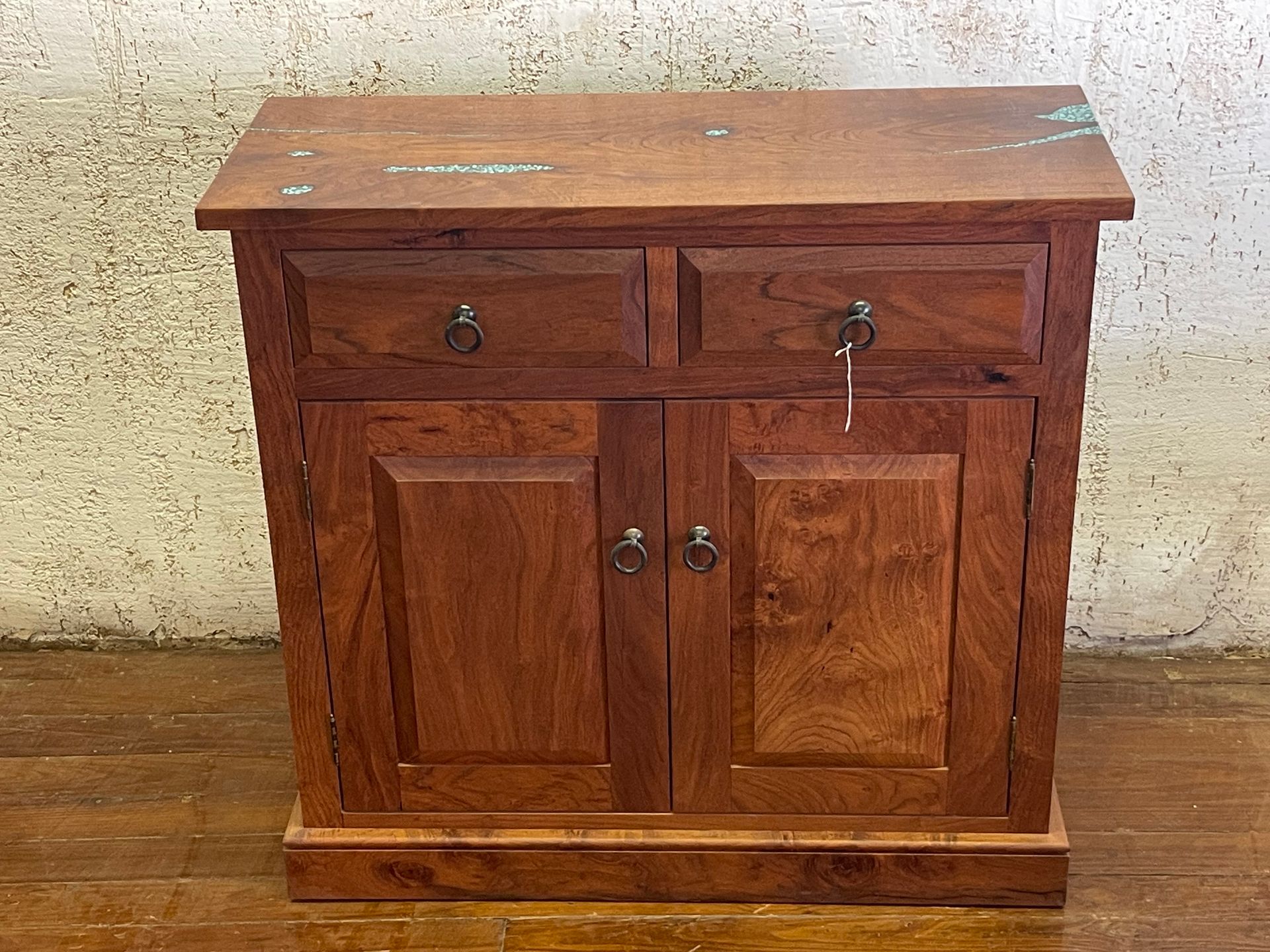 Small wooden cabinet with two drawers and double doors against a textured wall.