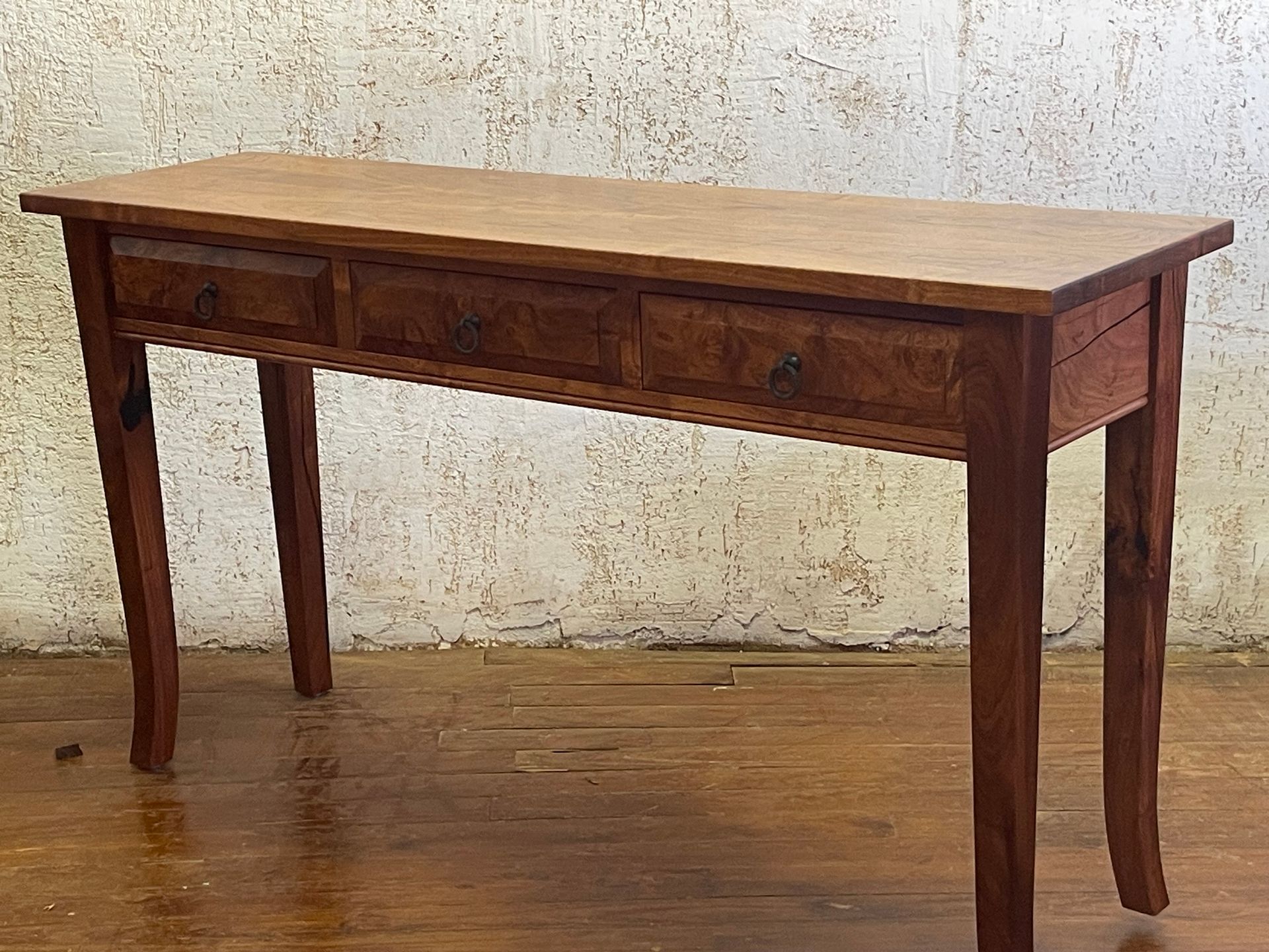Wooden antique-style desk against a textured wall on a hardwood floor