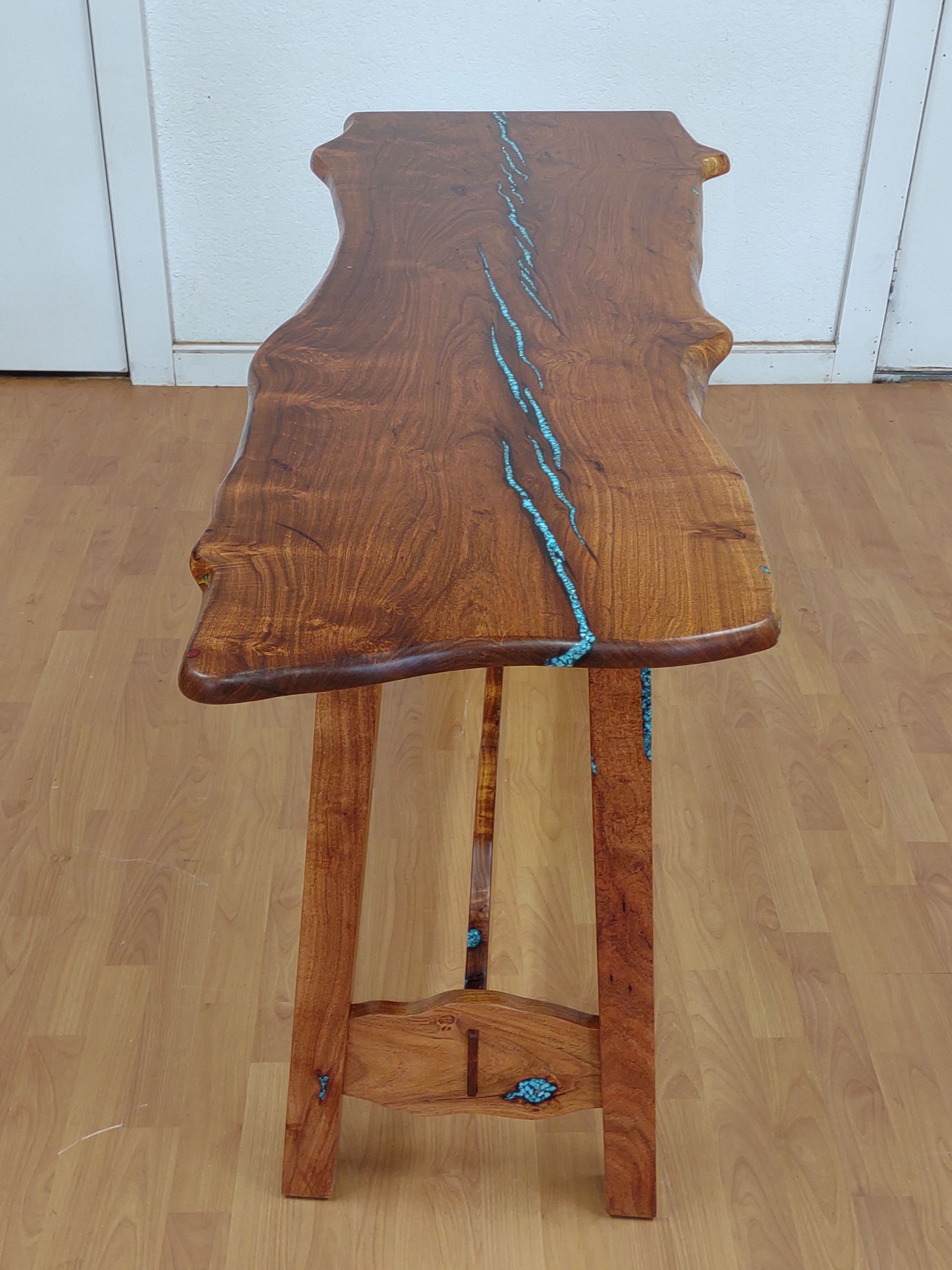 Rustic wooden stool with a live-edge top and blue resin inlay, standing on a wooden floor.