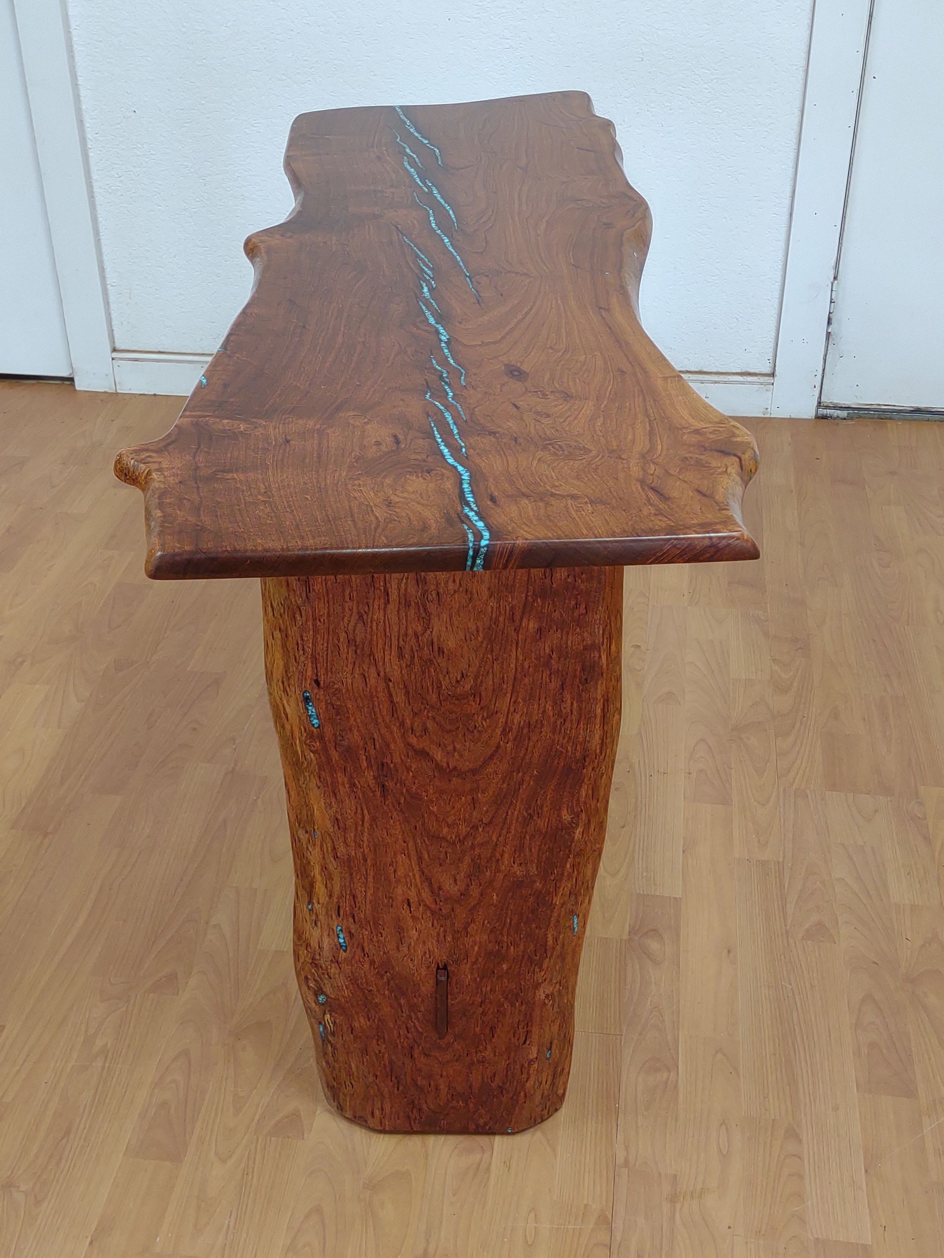 Rustic wooden bench or stool with a blue rope detail, standing on a wooden floor against white doors.