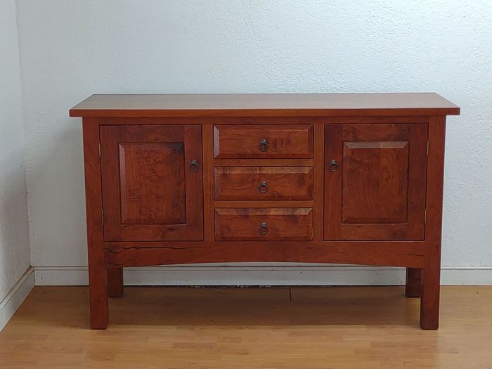 Wooden sideboard cabinet with drawers and doors against a white wall.