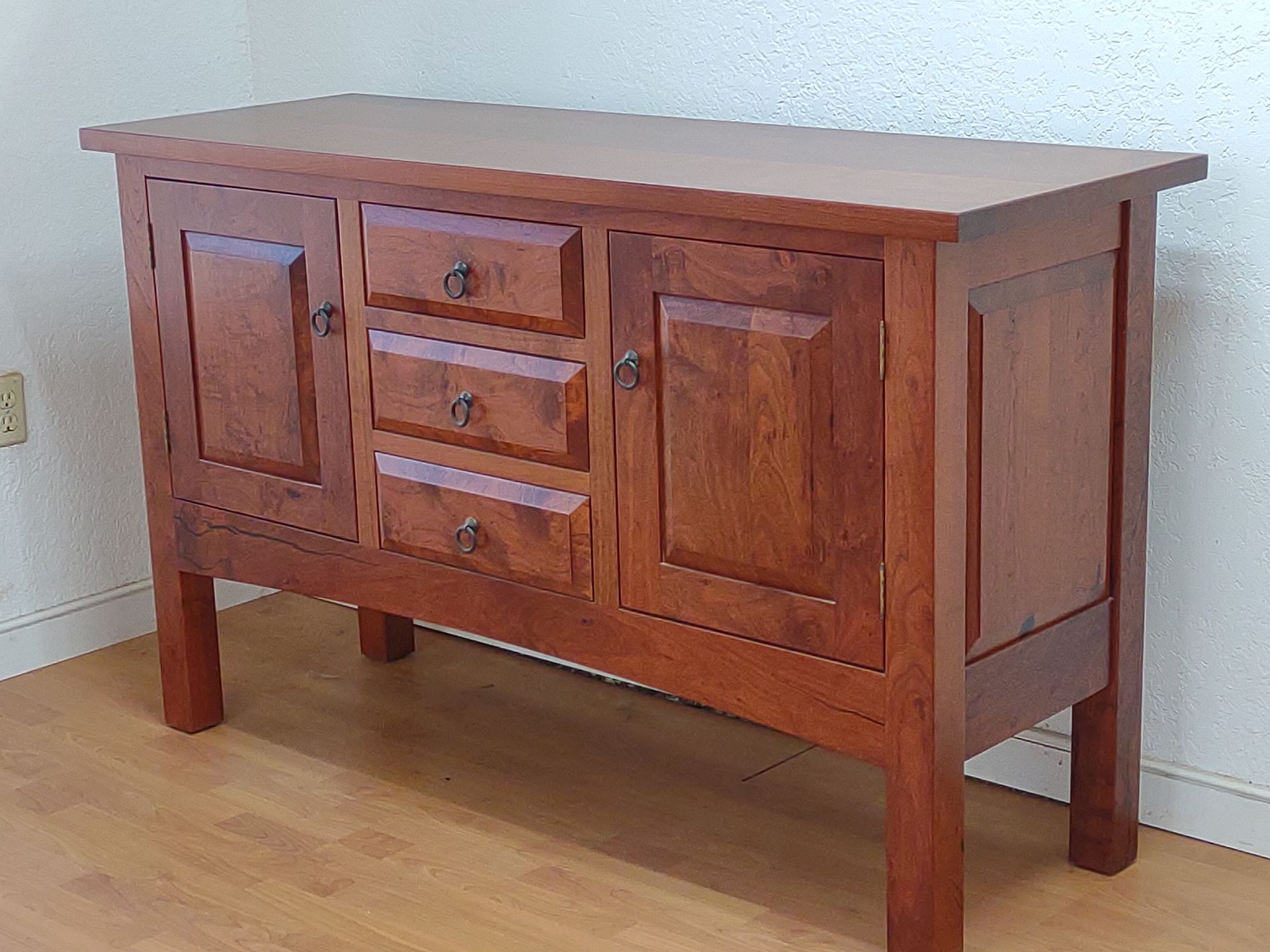 Wooden sideboard cabinet with drawers and doors on a light wood floor against a white wall