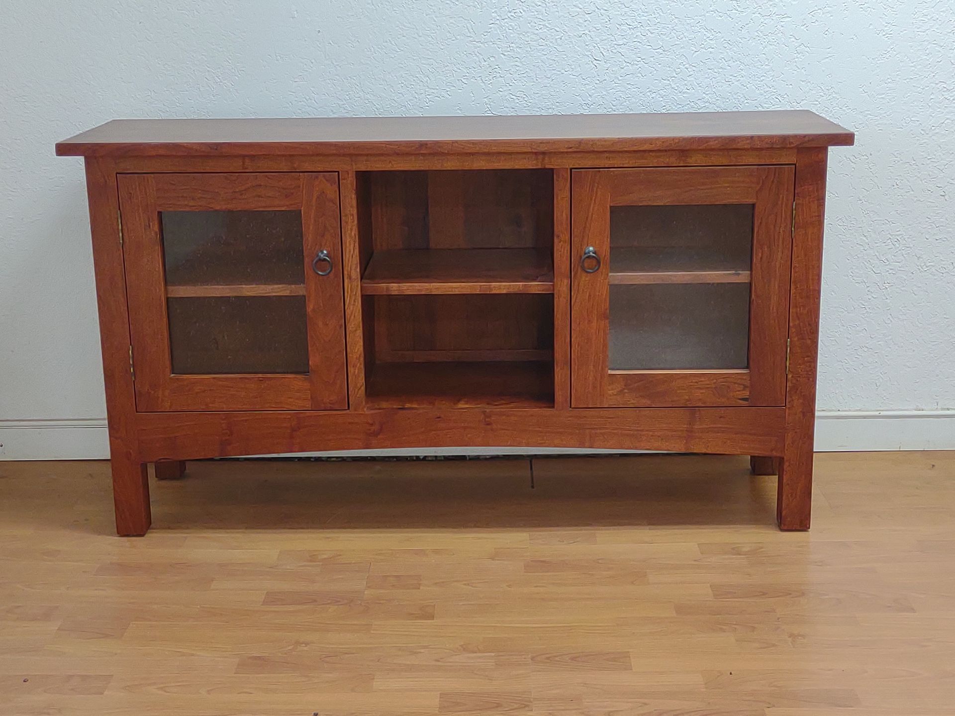 Wooden cabinet with glass doors and open center shelves against a plain wall