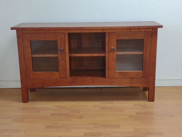 Wooden cabinet with two glass doors and a central open shelf against a plain wall.