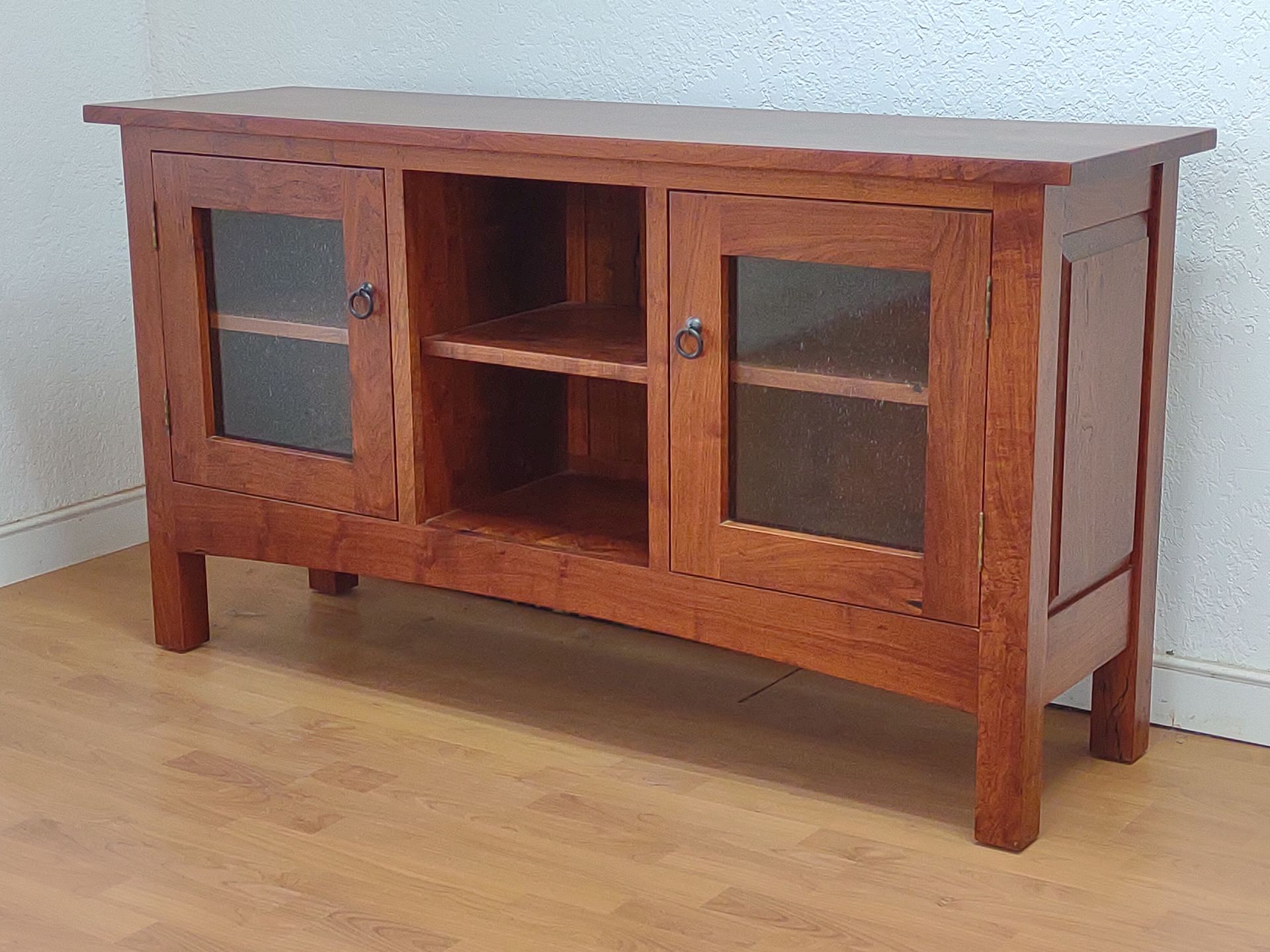 Wooden cabinet with glass doors and a central open shelf against a white wall.