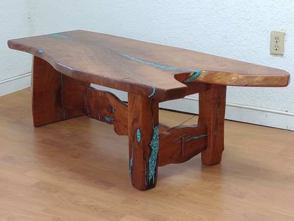 Wooden live-edge bench with turquoise accents on a hardwood floor against a white wall.