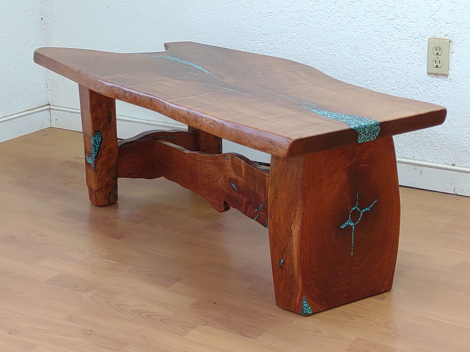 Rustic wooden bench with turquoise inlays on a light wood floor against a white wall.