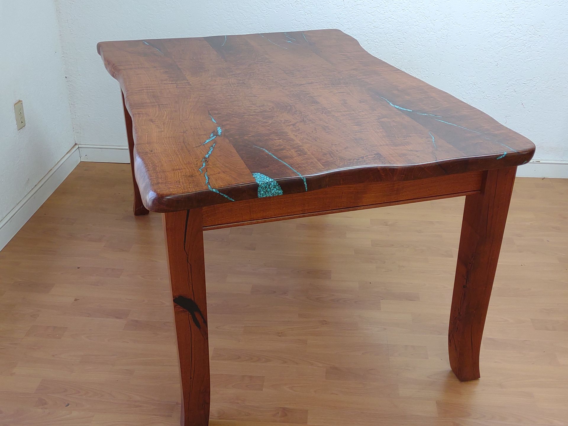 Small wooden table with a dark brown finish in an empty room, showing a slight crack on the top.