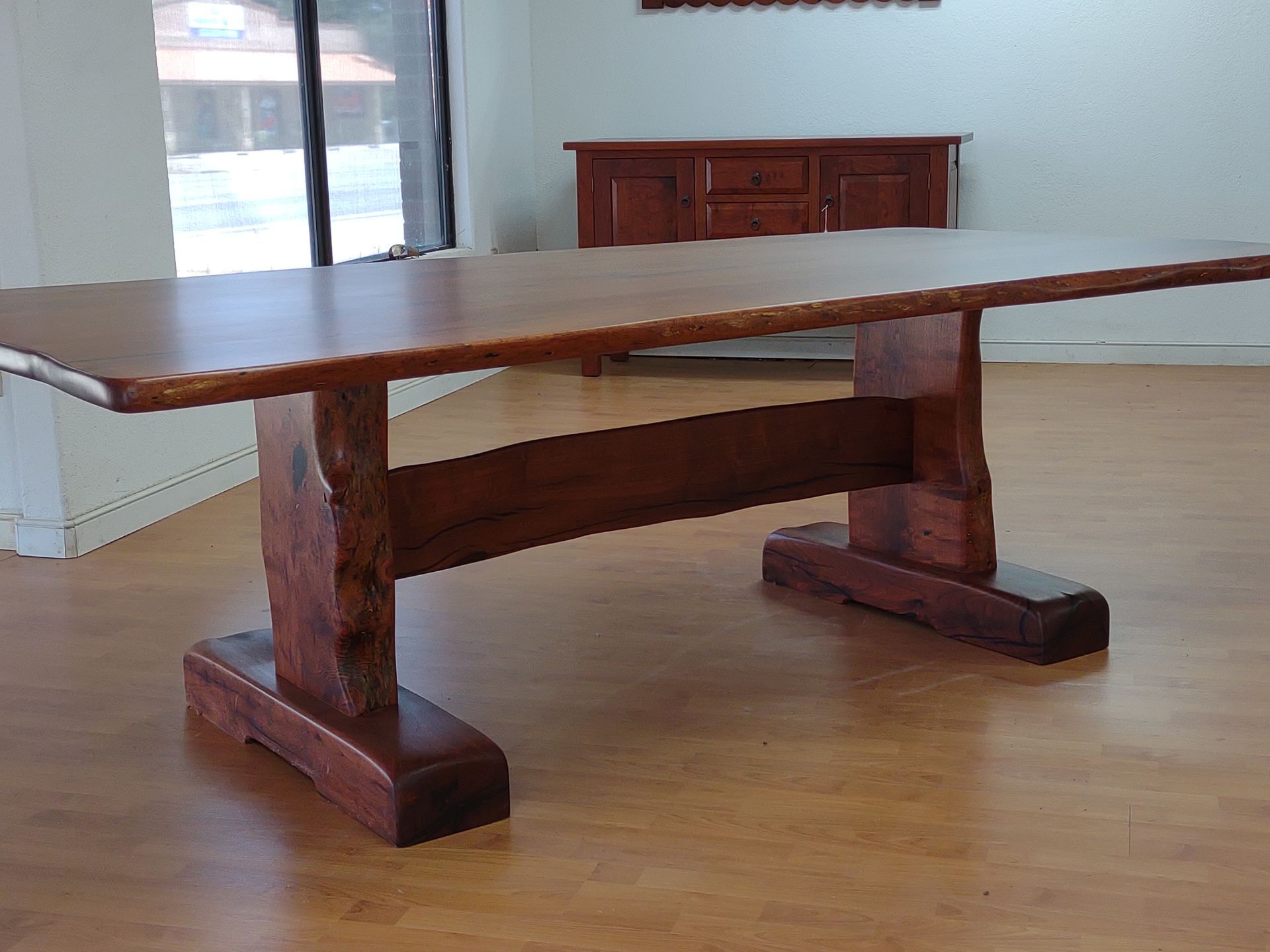 Rustic wooden dining table with thick carved legs in a bright, empty room.