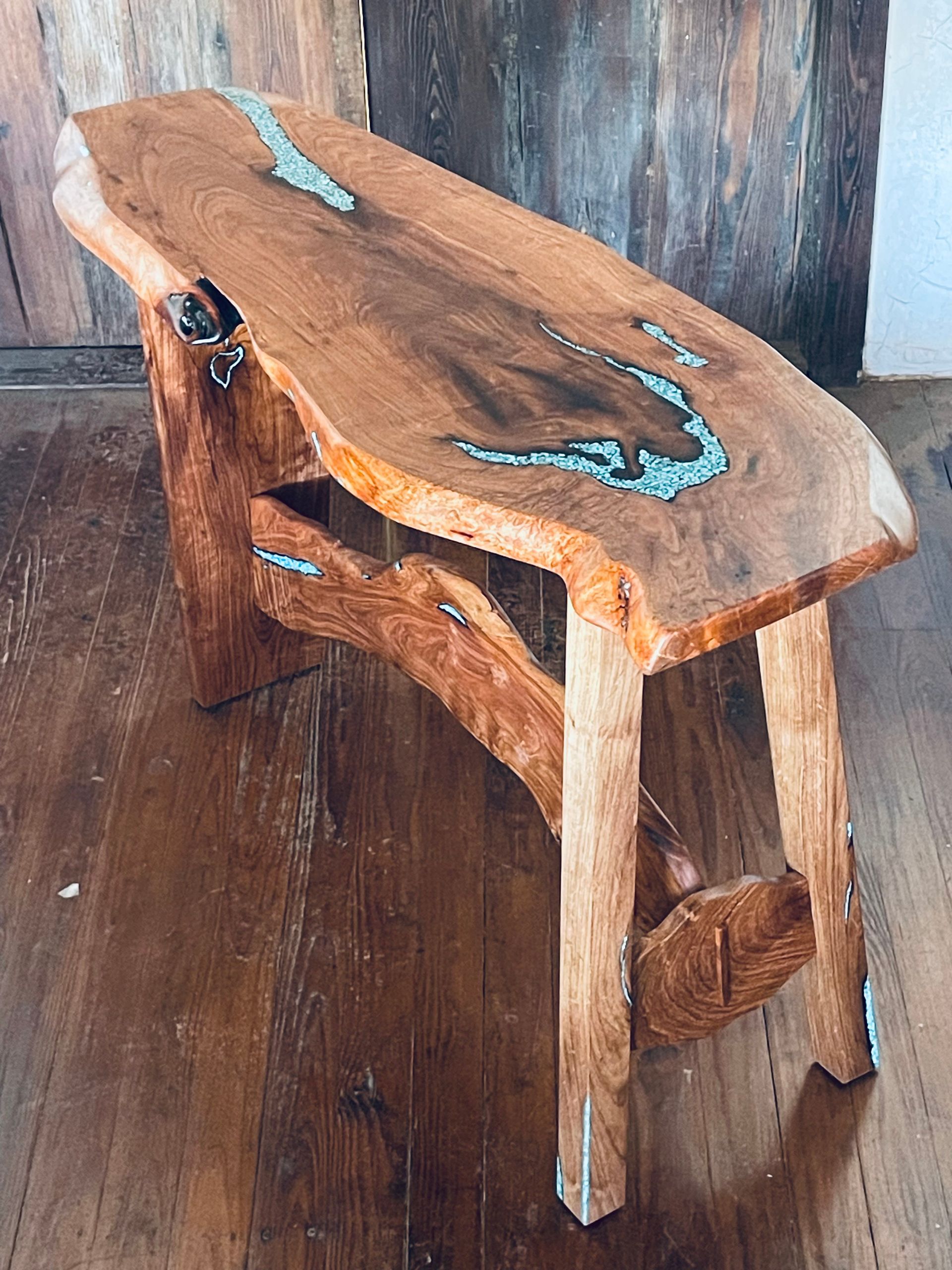 Rustic wooden bench with turquoise inlay accents on a dark floor against a wood wall.