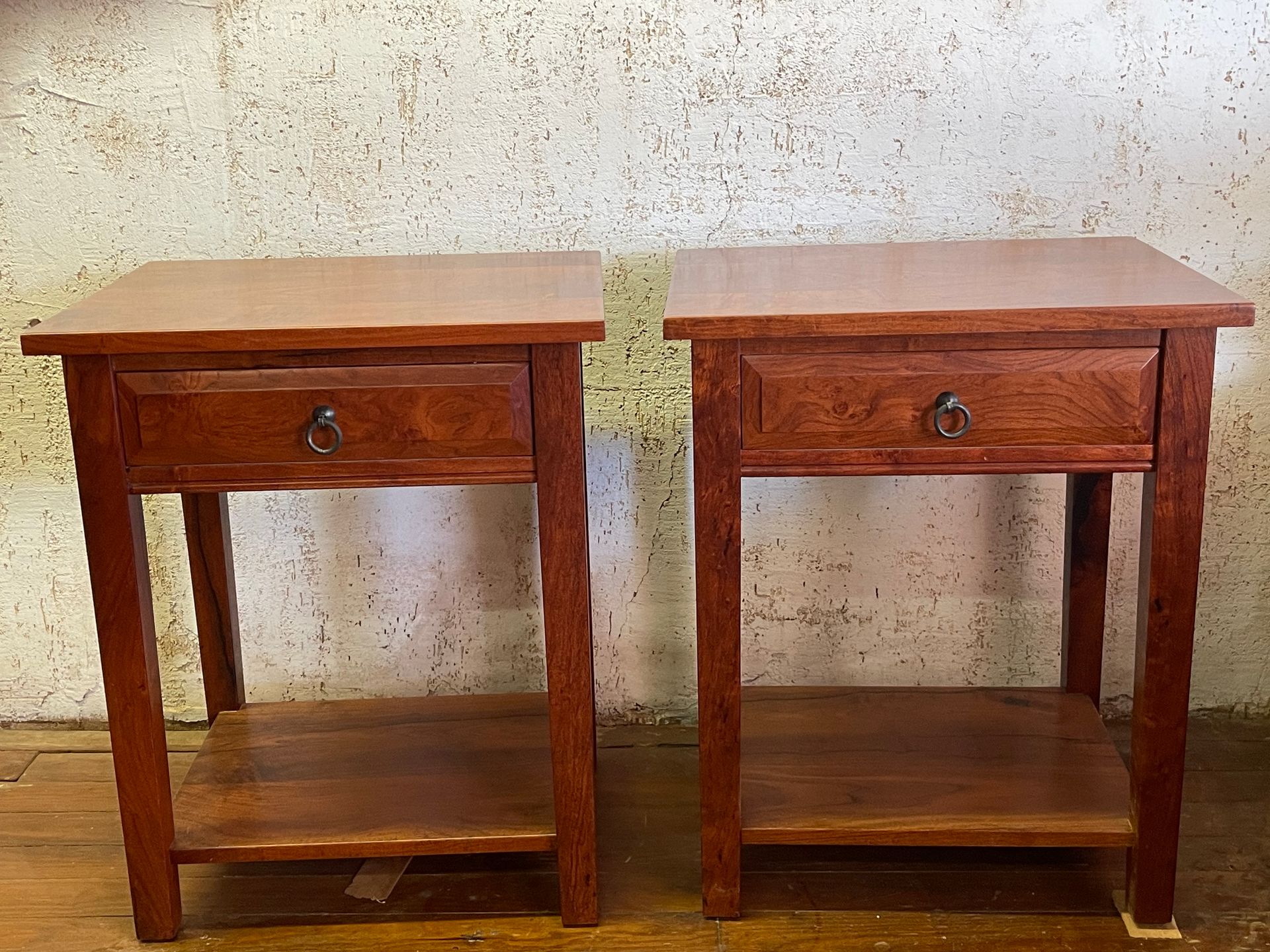 Two small wooden side tables with drawers against a textured wall.