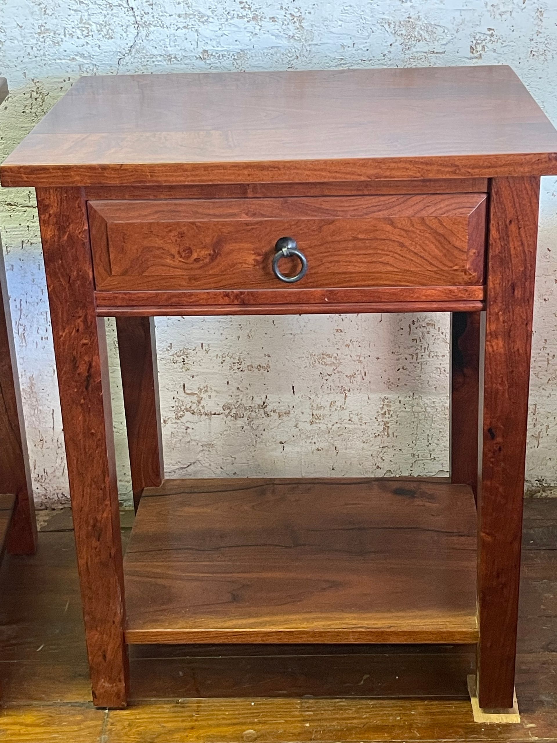 Wooden bedside table with a drawer and lower shelf against a worn wall.