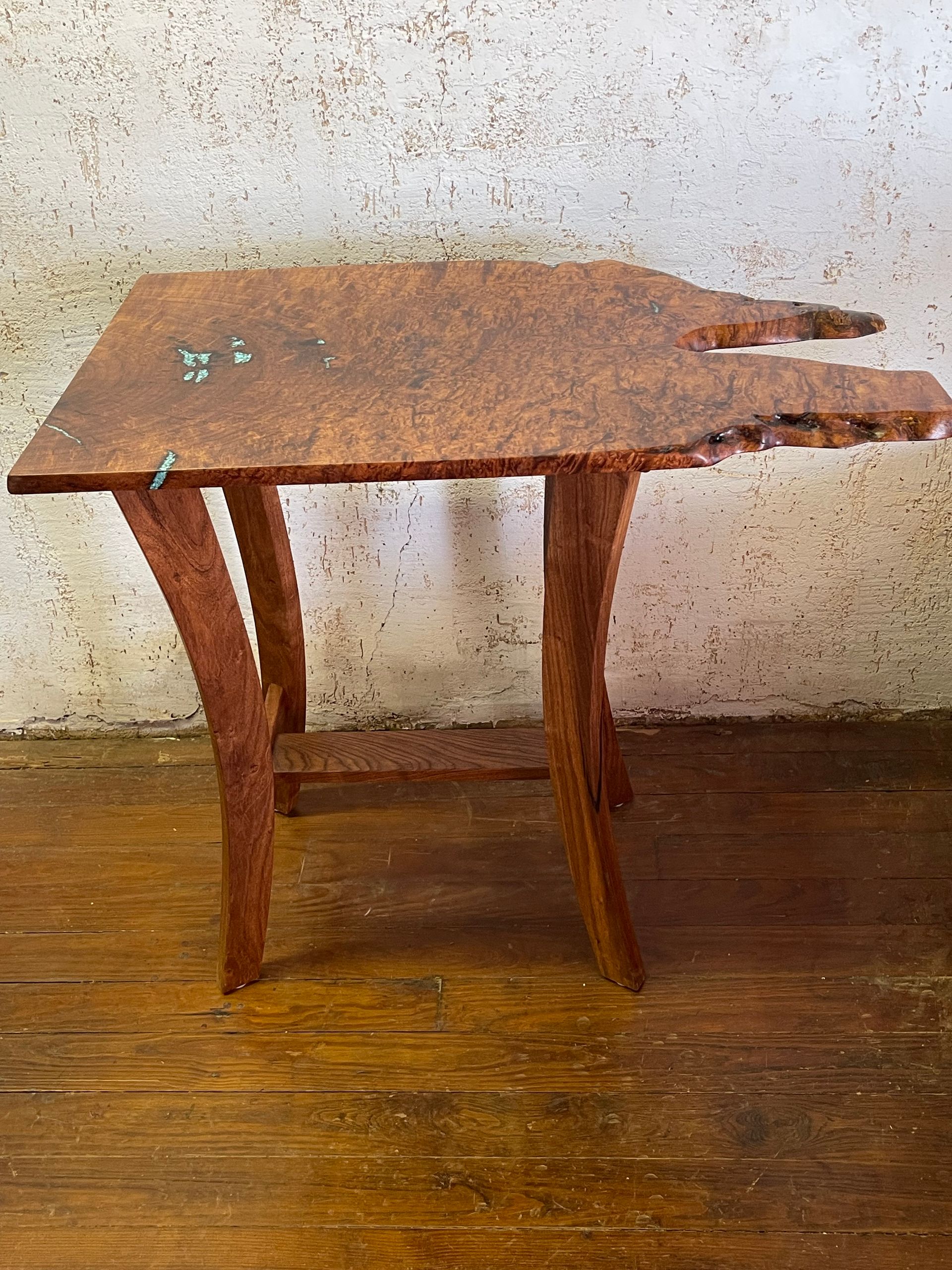Rustic wooden table with an irregular, chipped top and curved legs against a plain wall.