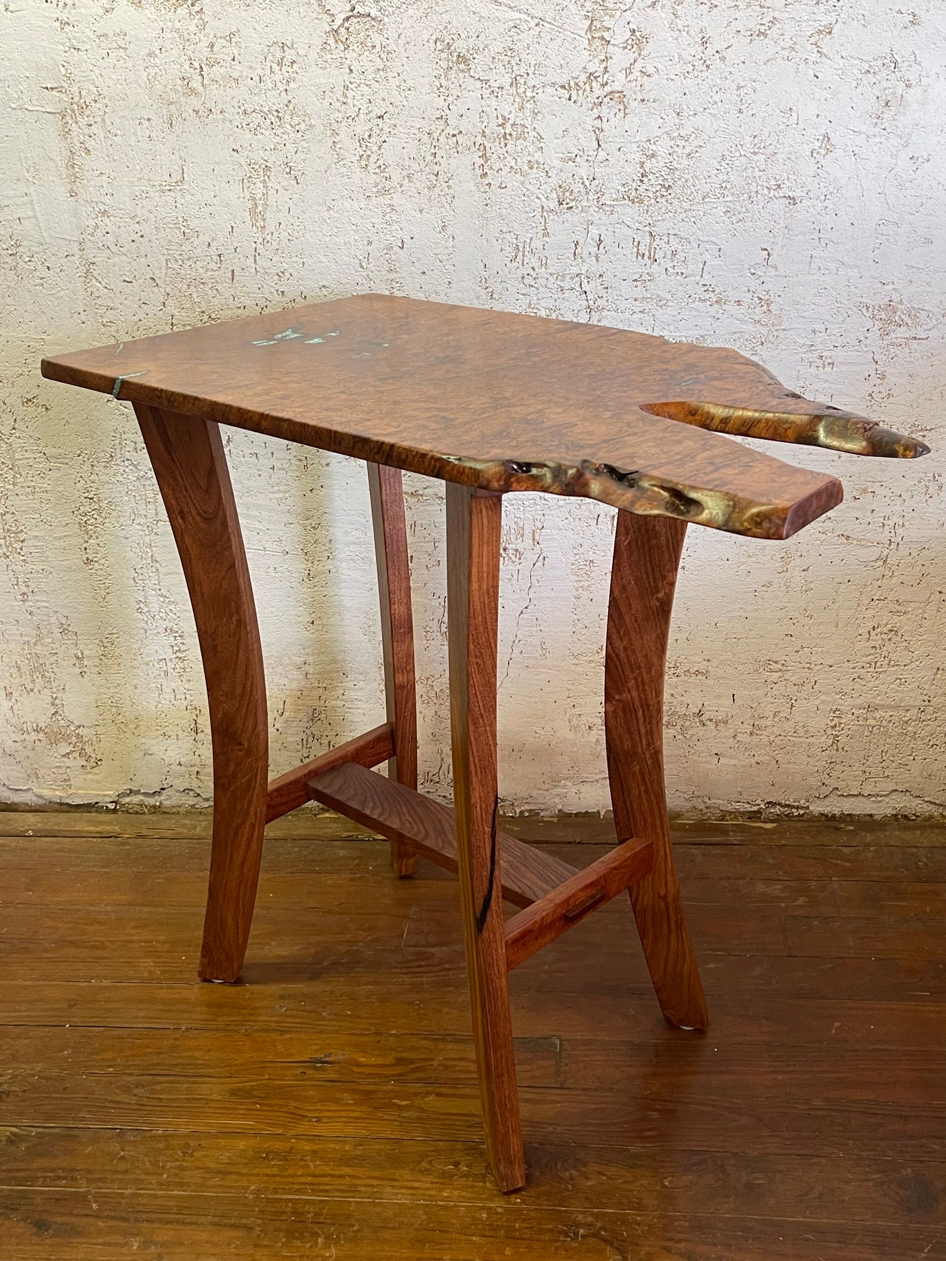 Rustic wooden table with a cracked top and tapered legs on a worn floor against a textured wall