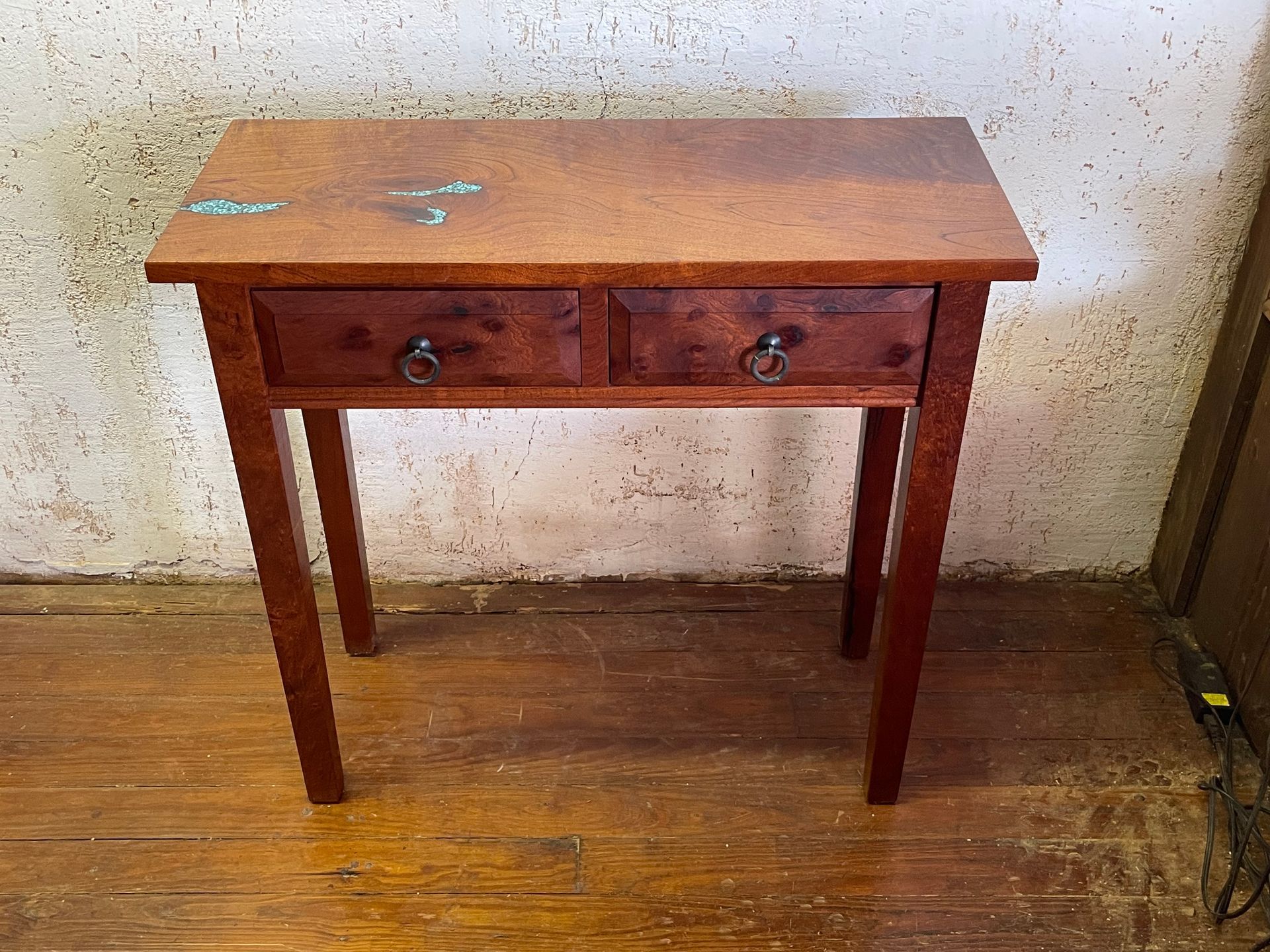 Small wooden table with two drawers in a worn indoor room.