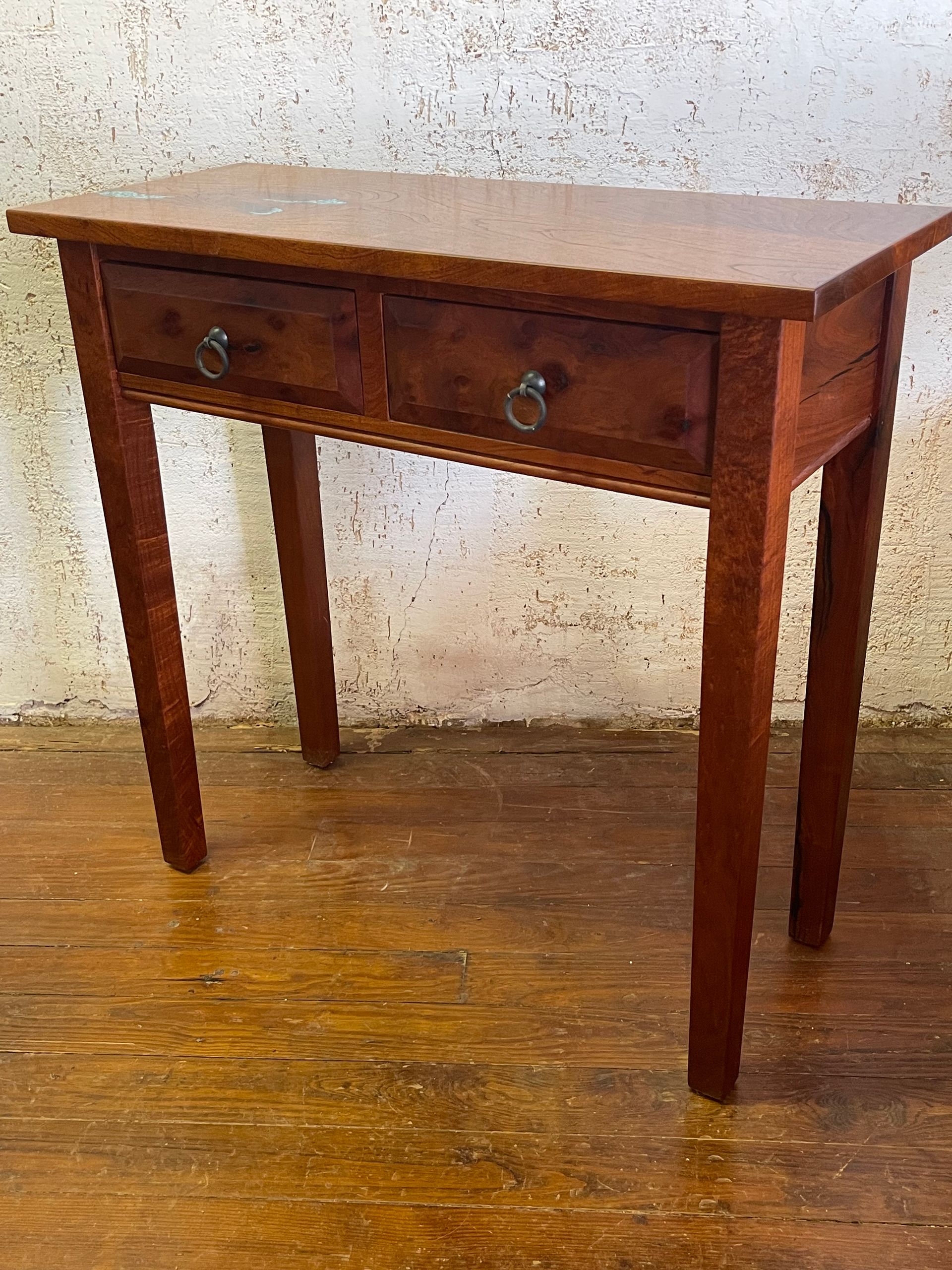 Small wooden console table with a drawer and two knobs on a wood floor against a speckled wall