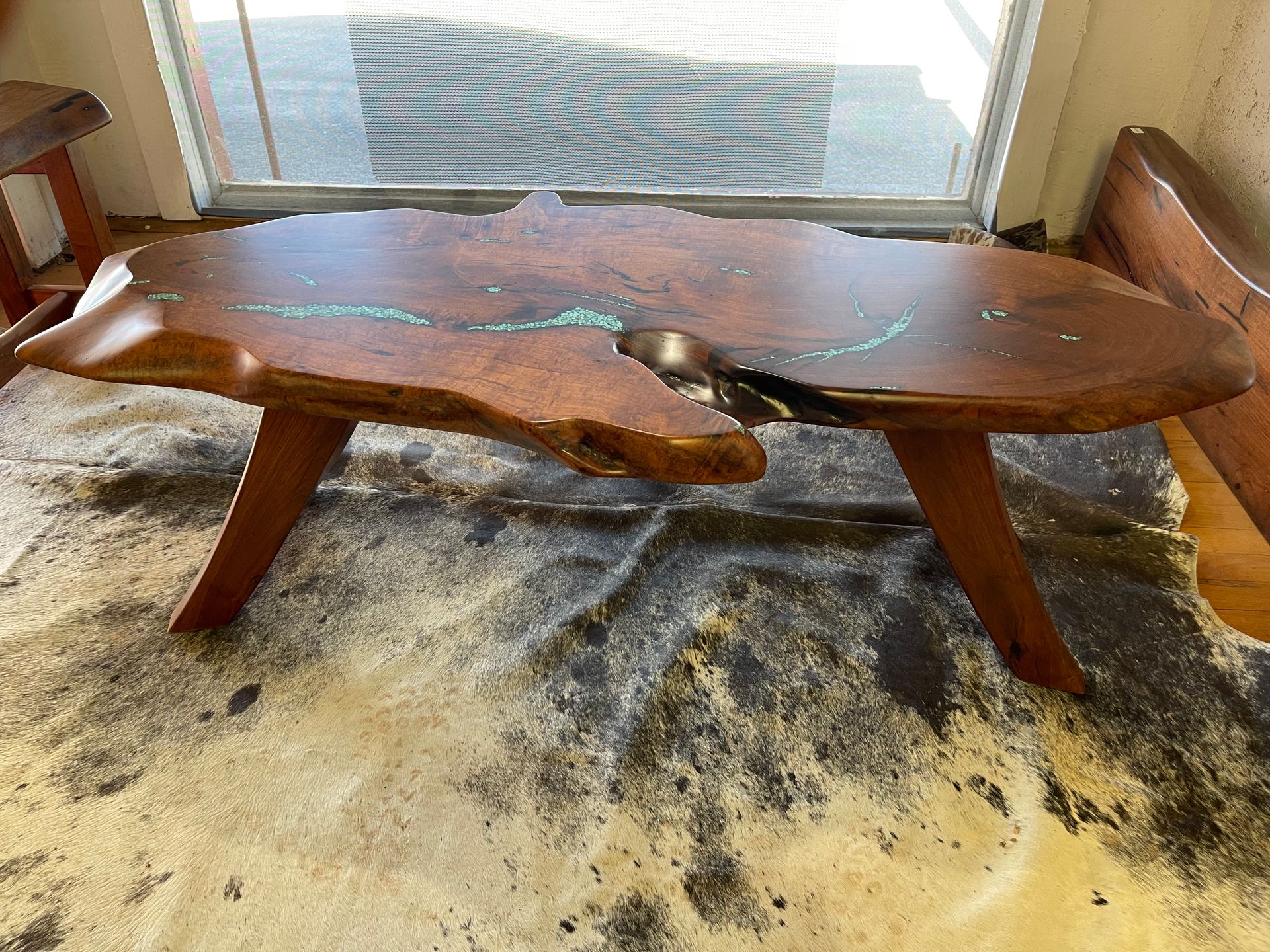 Rustic wooden bench table with carved seat in front of a window, on a patterned rug.