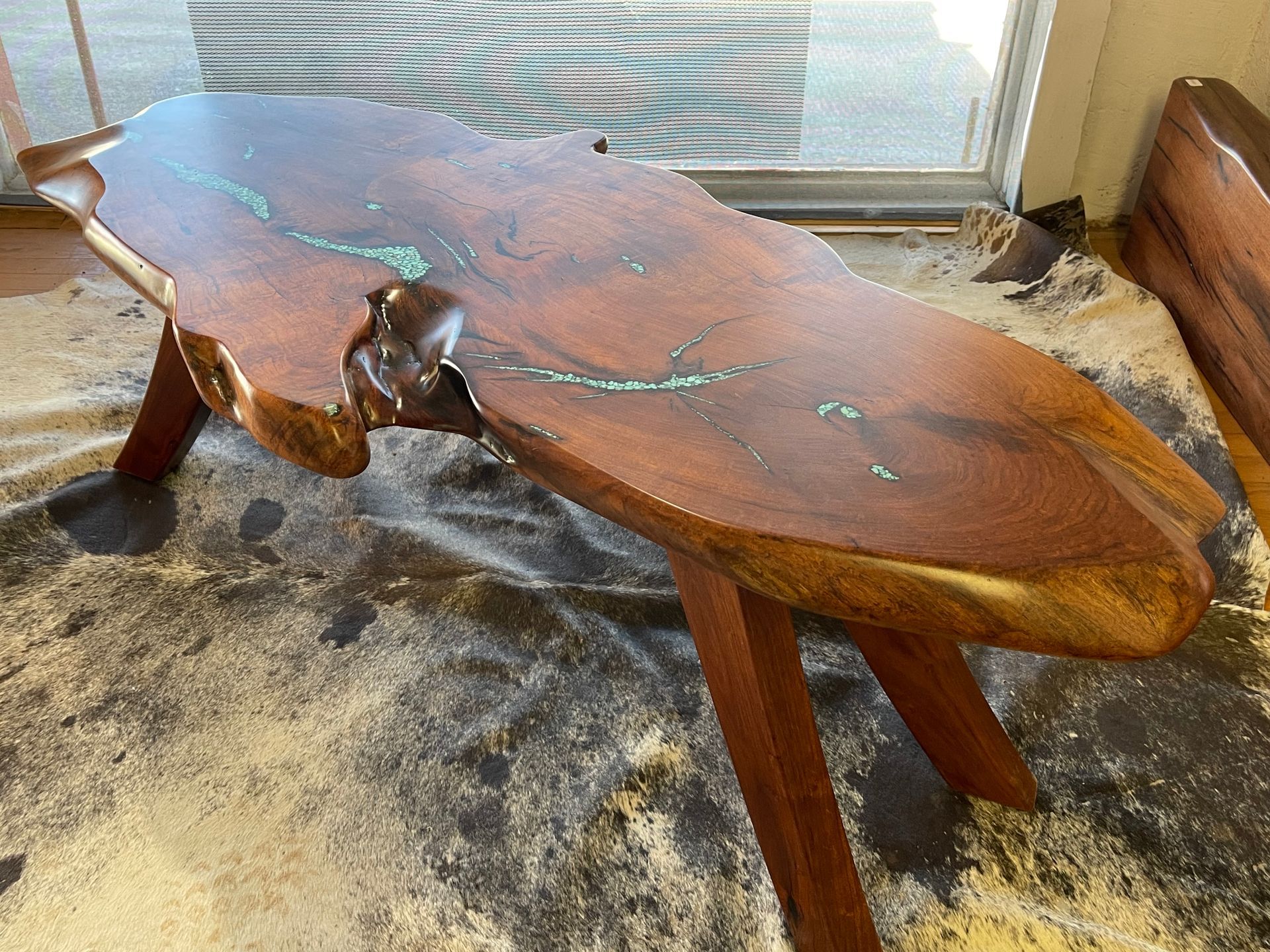 Rustic wooden coffee table with a live-edge top and green inlay accents, sitting on a carpeted floor.