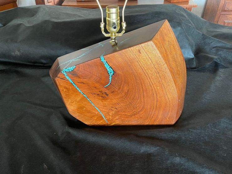 Small wooden geometric lamp base with a bright blue crack, hanging bulb above it.