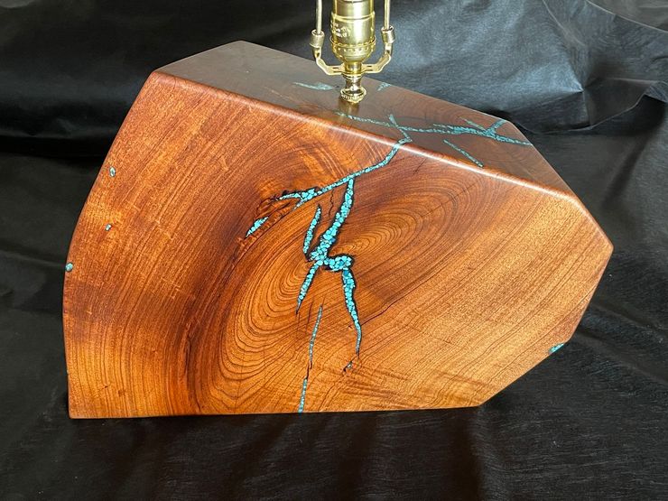Wooden block with turquoise resin crack, held under a metal tool against a black background