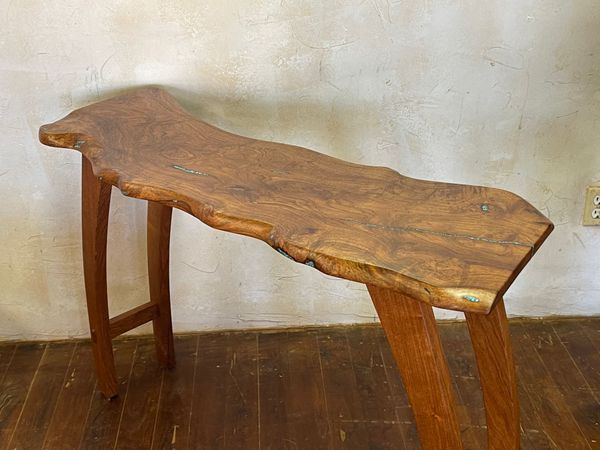 Rustic wooden stool with a natural edge top on a wooden floor against a plain wall